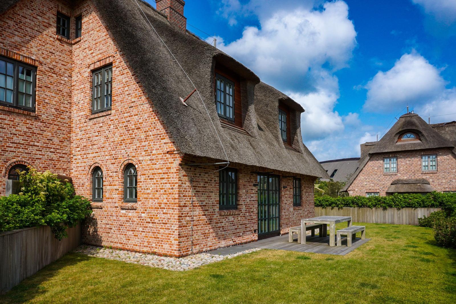 Red brick building with thatched roof and wooden terrace in the garden.