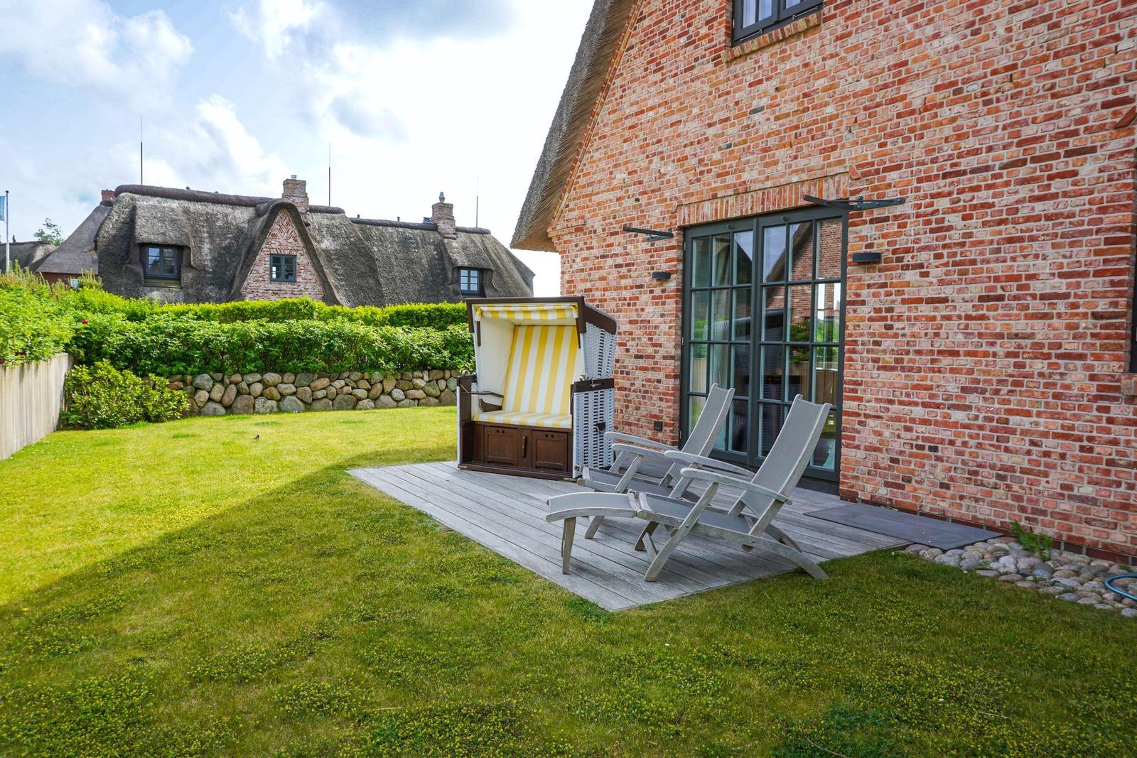 Red brick house with terrace, beach chair, and lounge chairs in the garden.