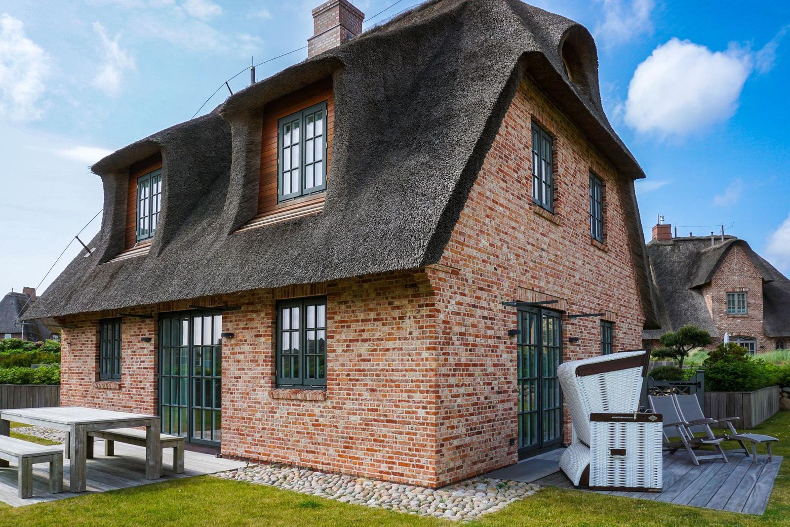 House with thatched roof and brick facade, garden area with table and seating.
