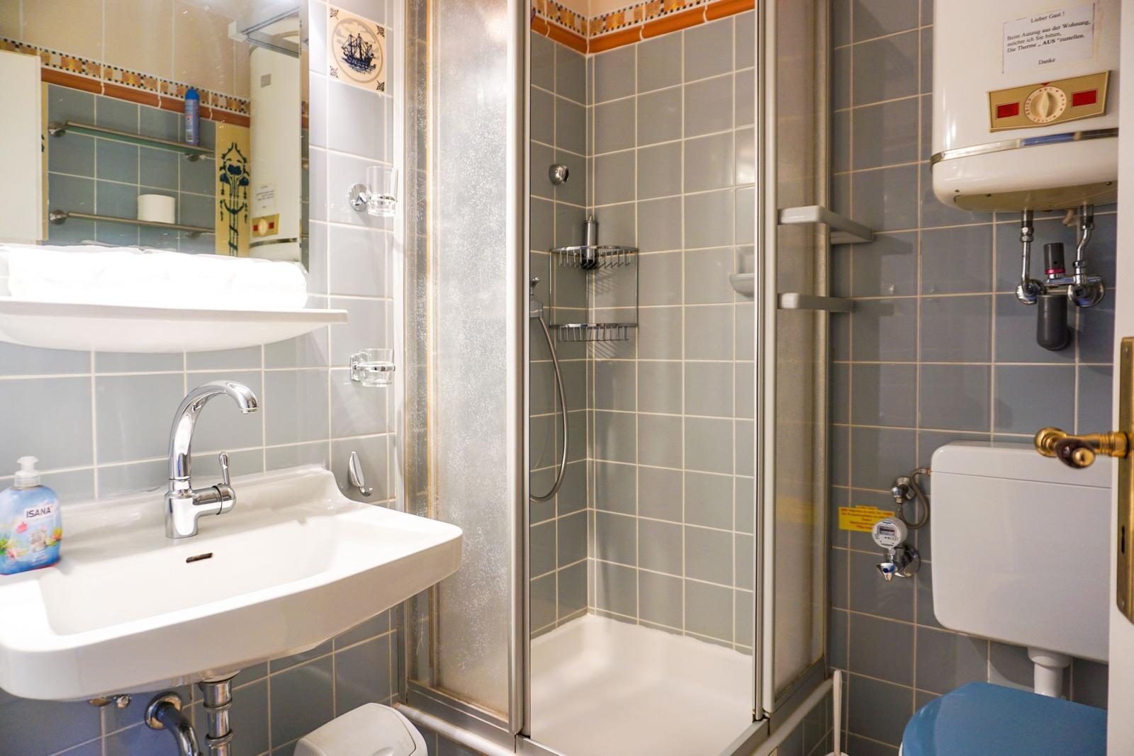 Badezimmer mit Dusche, Waschbecken und Toilette. Fliesenwand und Spiegel sichtbar.