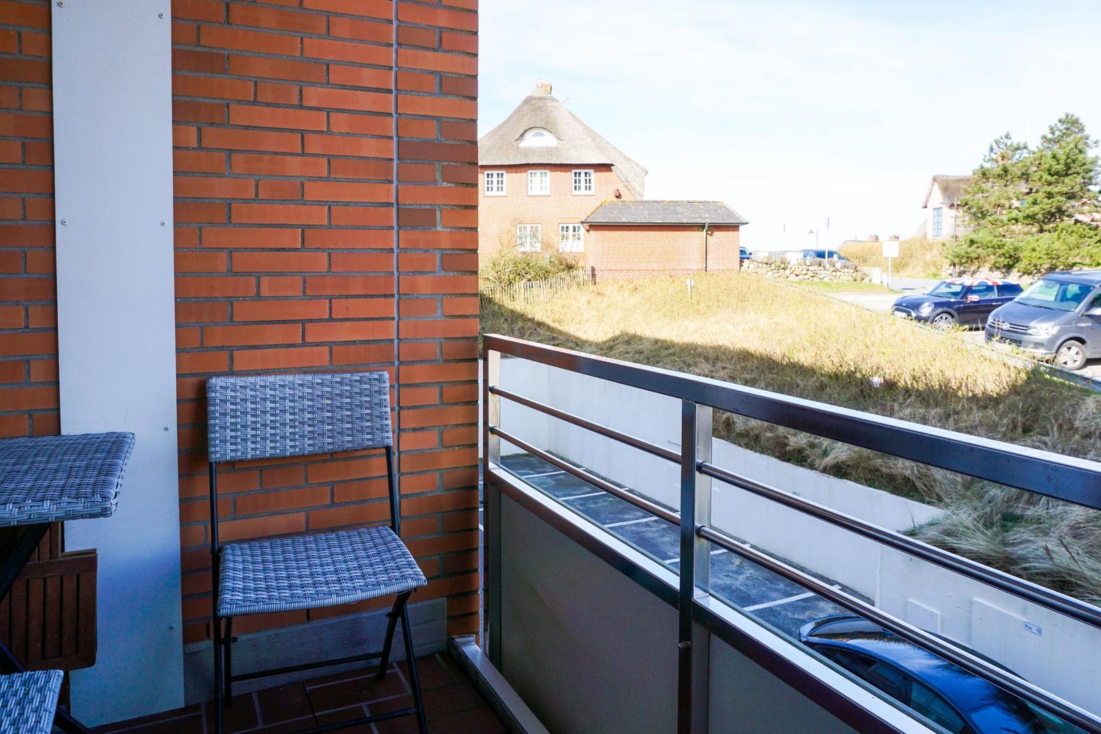 Balkon mit Stuhl und Tisch, Blick auf Haus und Grünfläche.