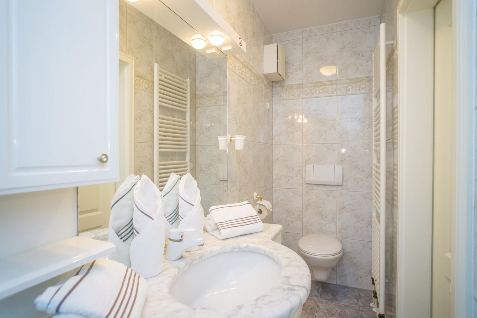 Badezimmer mit Marmor, Waschbecken, Toilette und Handtuchhalter.