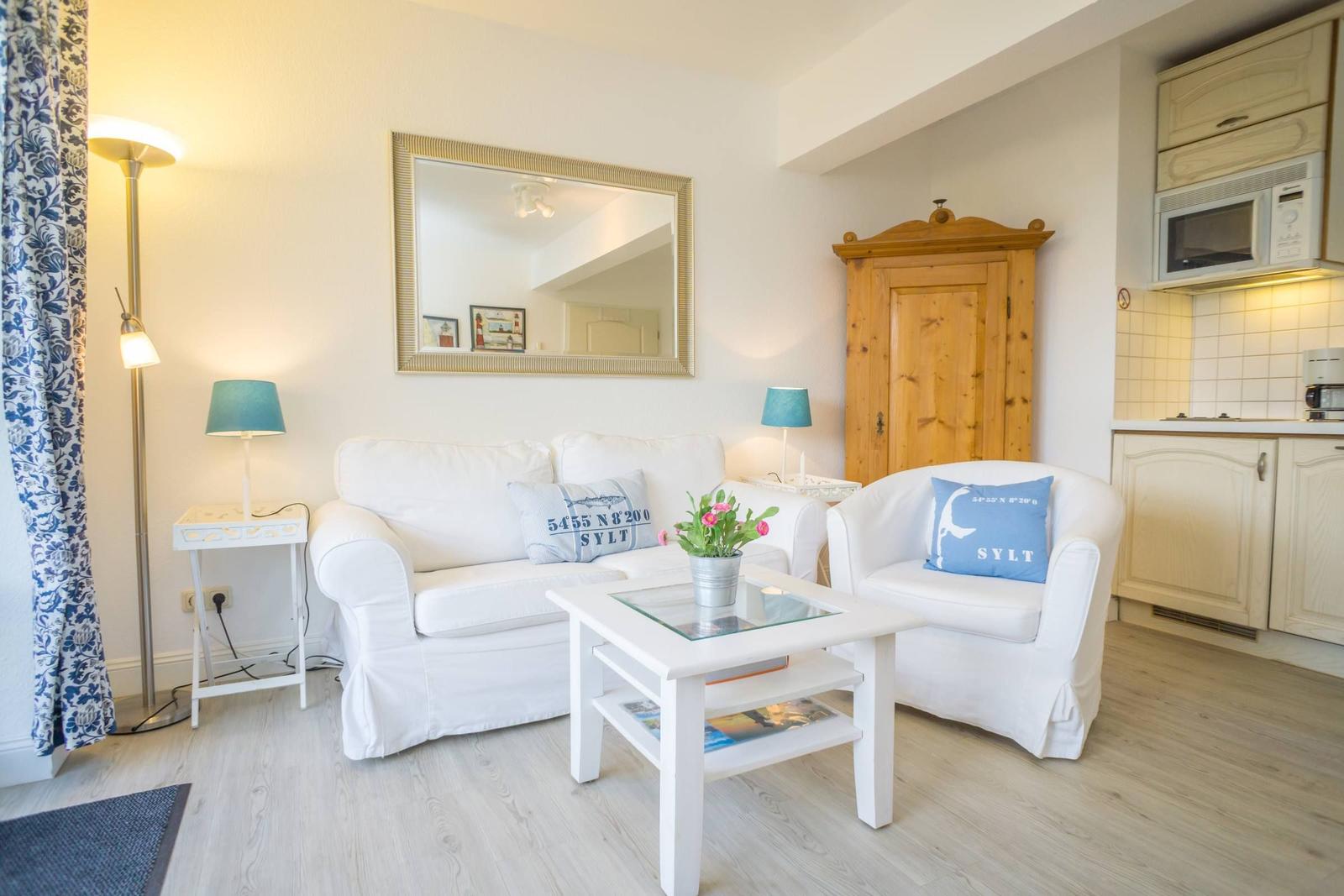 Wohnzimmer mit Sofa, Sessel und Küchenbereich. Holzfußboden und Spiegel an der Wand.