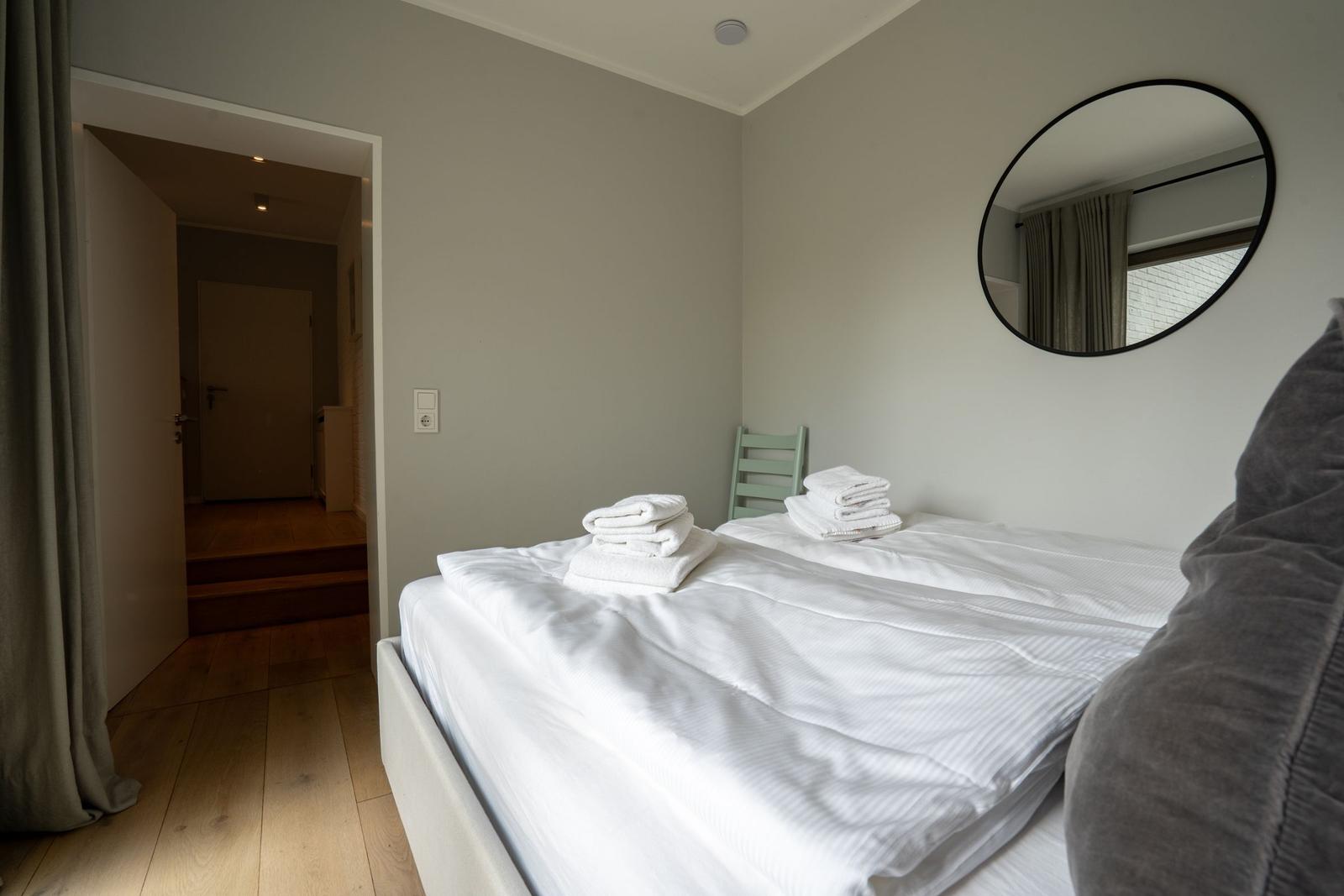 Schlafzimmer mit Bett, Handtüchern und runden Spiegel an der Wand.