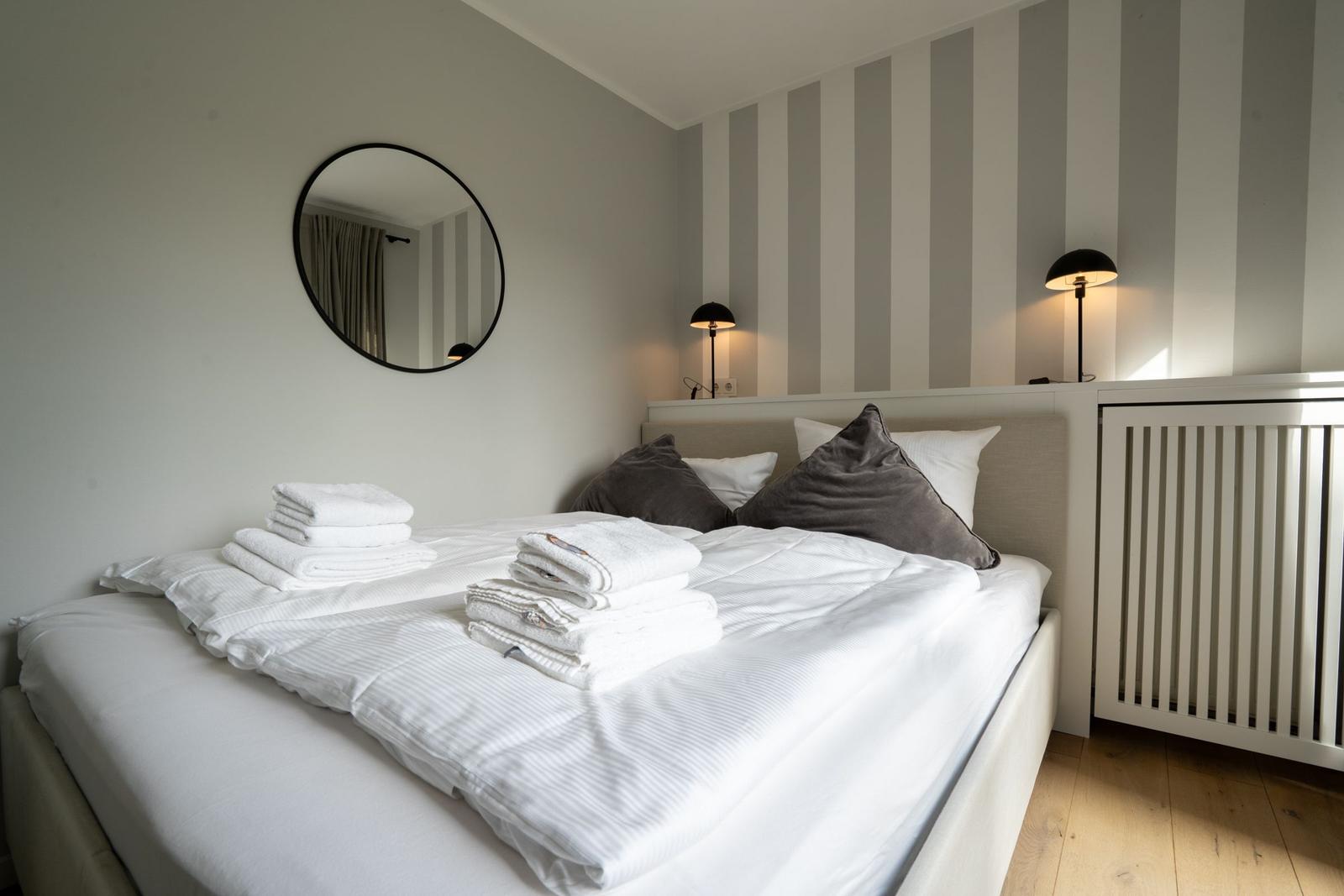Schlafzimmer mit Bett, Handtüchern, Spiegel und Lampe an der Wand.