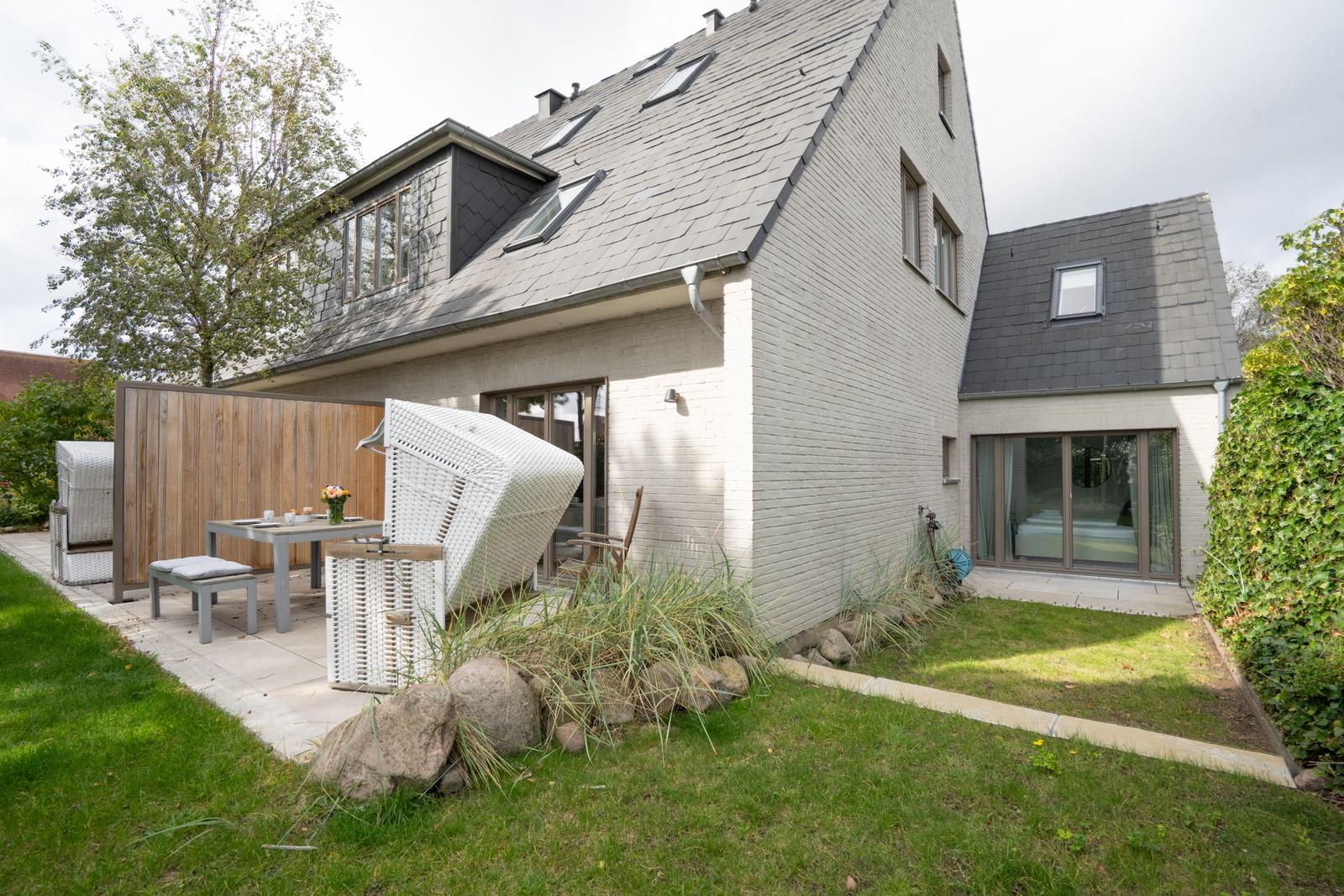 Moderne Villa mit Garten, Terrasse und weißen Rattanmöbeln.