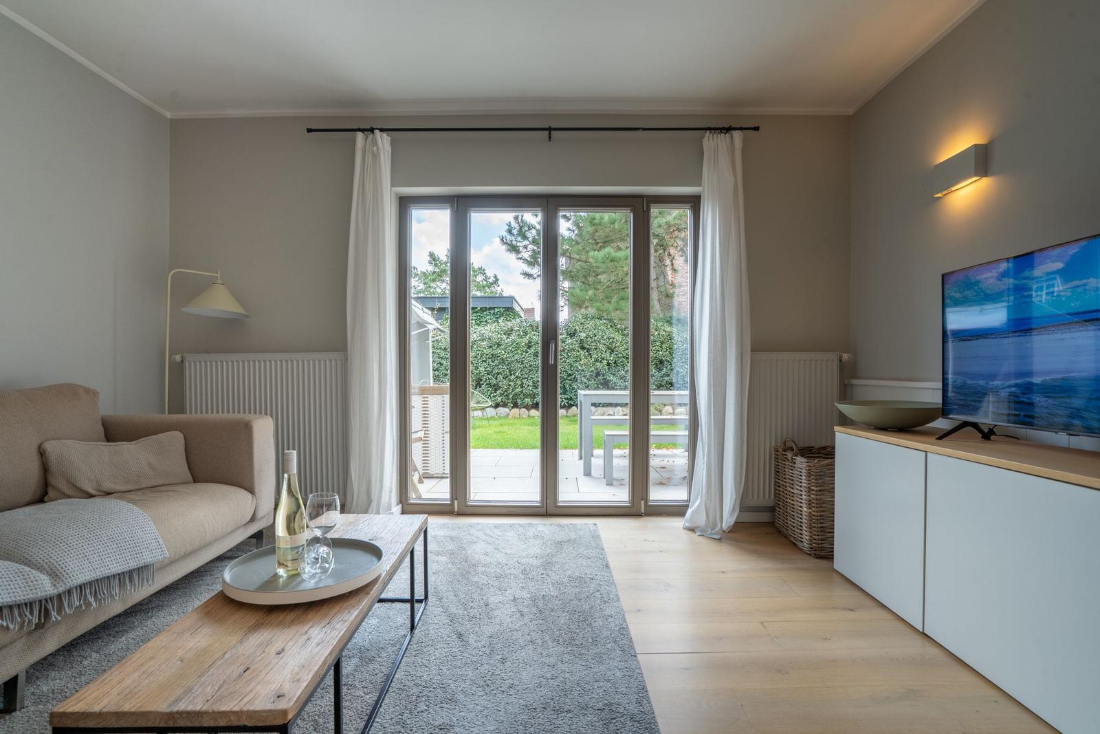 Wohnzimmer mit Sofa, Couchtisch und TV. Durchgang zur Terrasse mit Gartenansicht.