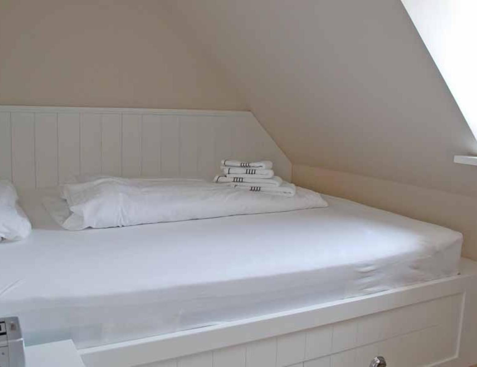 Bedroom with white bed and stacked towels under sloped ceiling