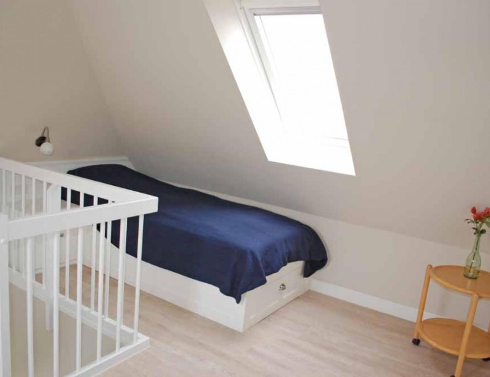 A bedroom with sloped ceiling, bed, crib, and window.