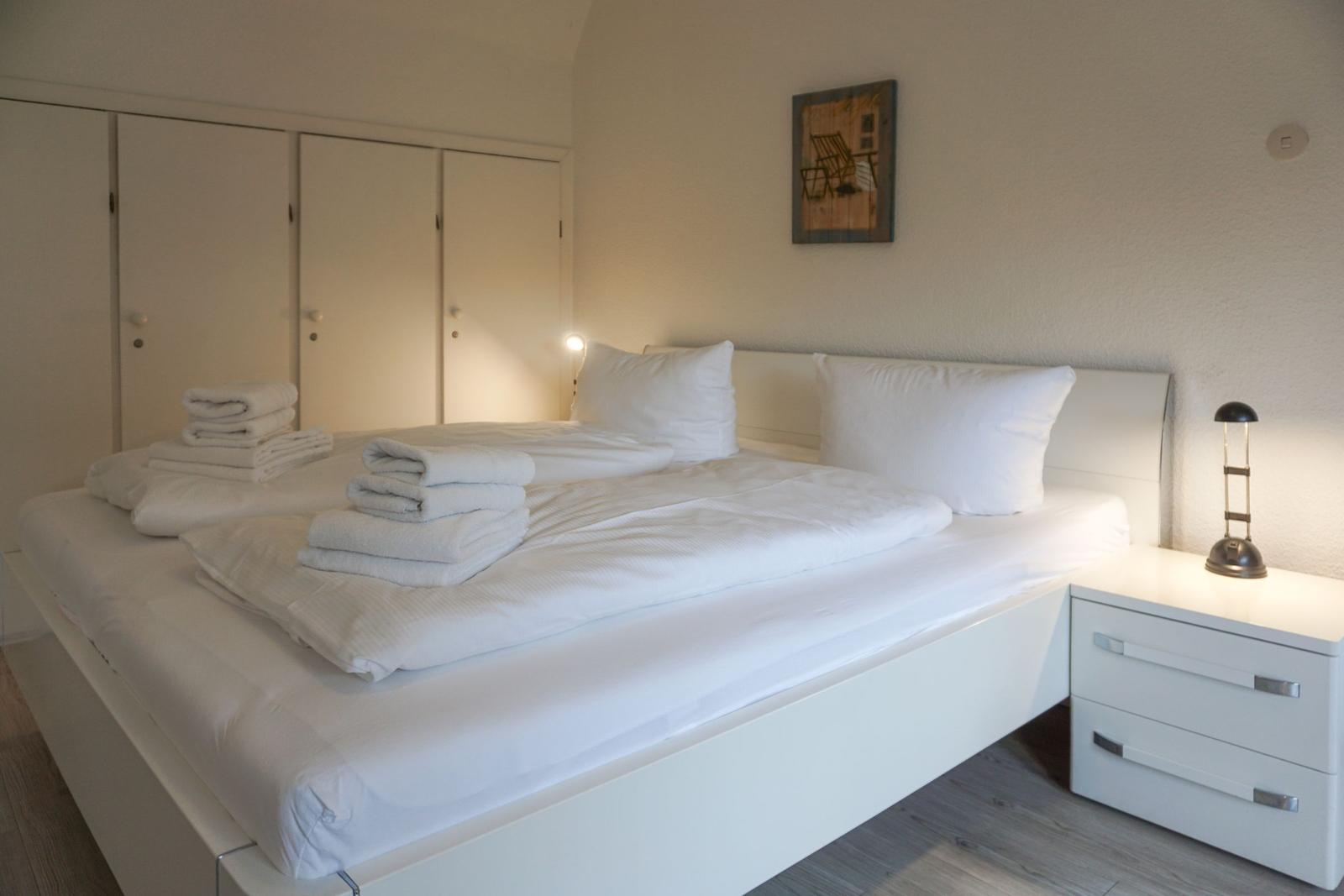 Schlafzimmer mit weißem Bett, Nachttisch und Kleiderschrank.