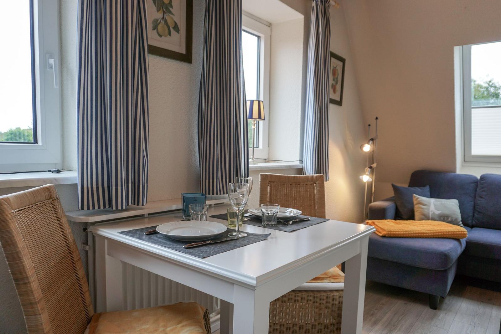 Esszimmer mit Tisch und Stühlen, Sofa und Fenstern mit Vorhängen.