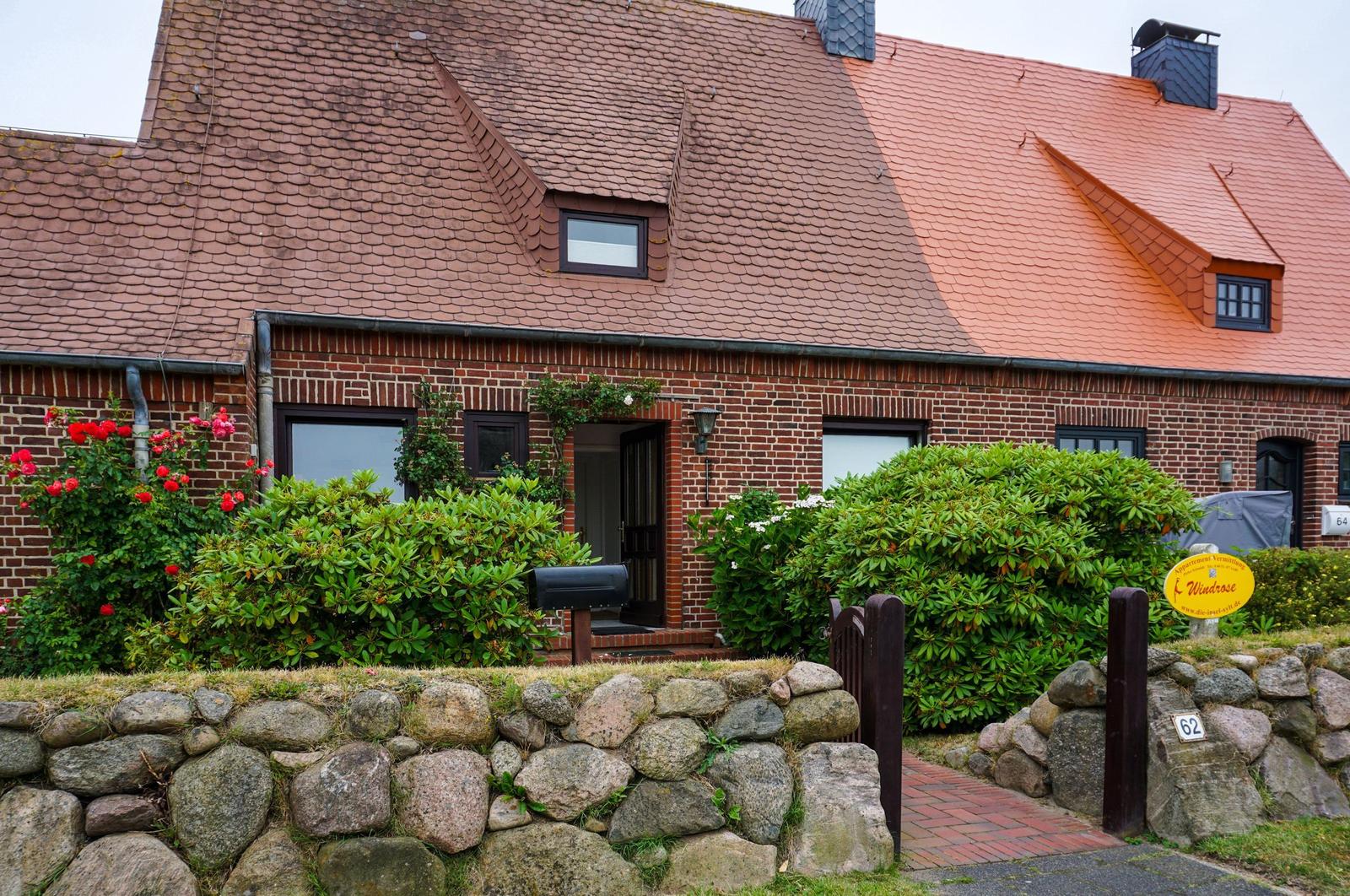 Rotes Ziegeldach, Backsteinhaus mit Eingang und grünen Sträuchern.