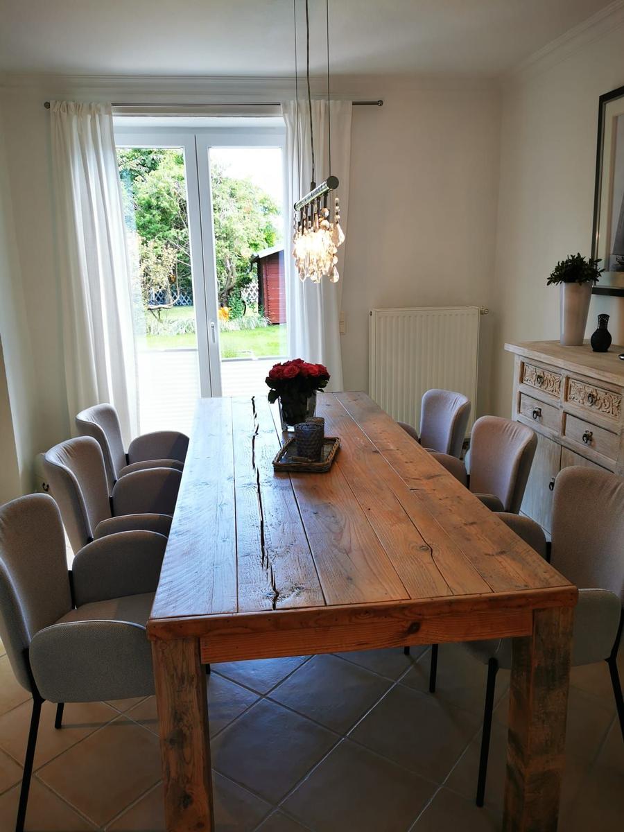 Esszimmer mit massivem Holztisch und Stühlen, Glasfront zum Garten, Hängelampe und Sideboard.