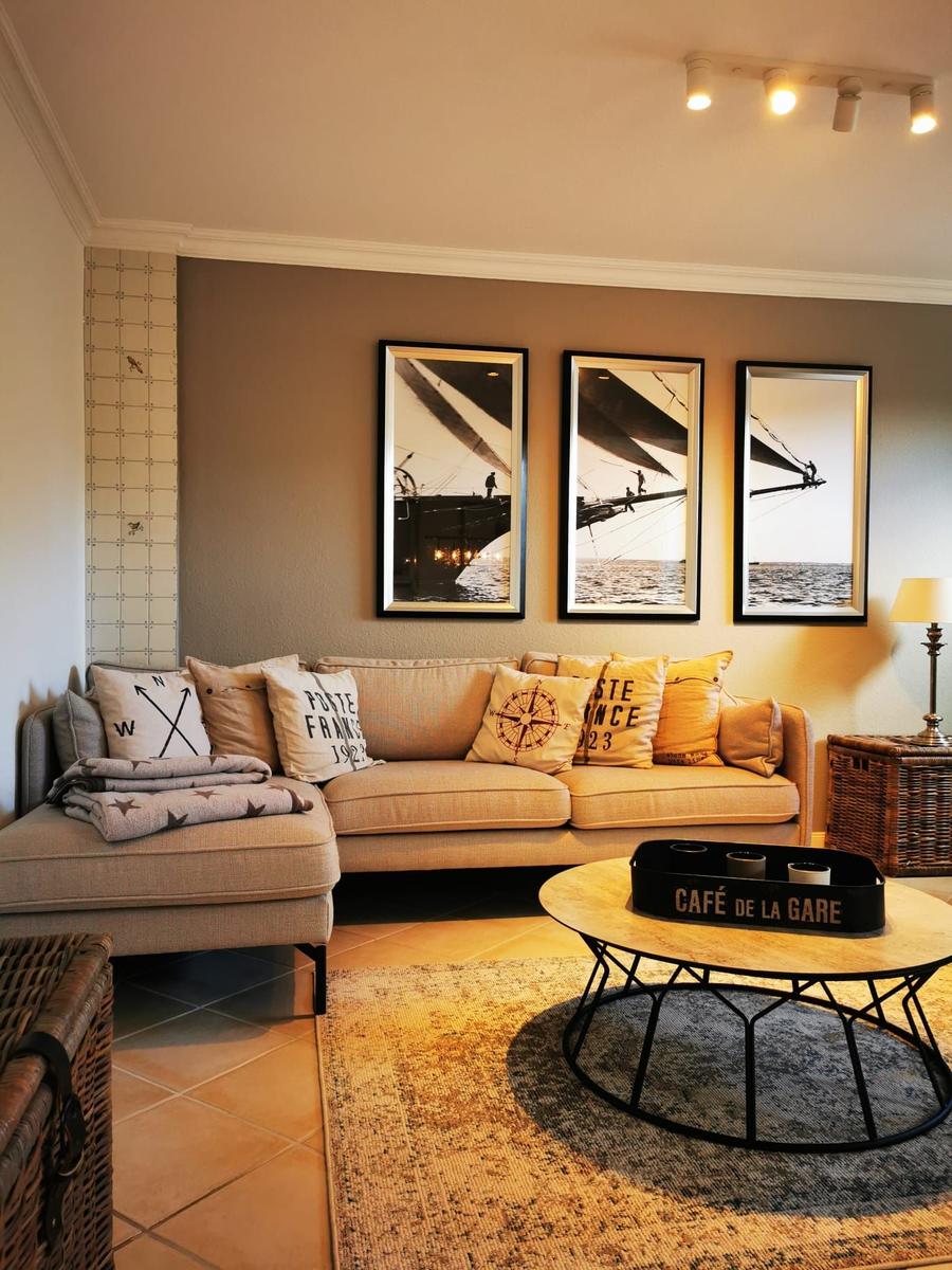 Wohnzimmer mit Sofa, Kissen, Wandbildern und runden Tisch.