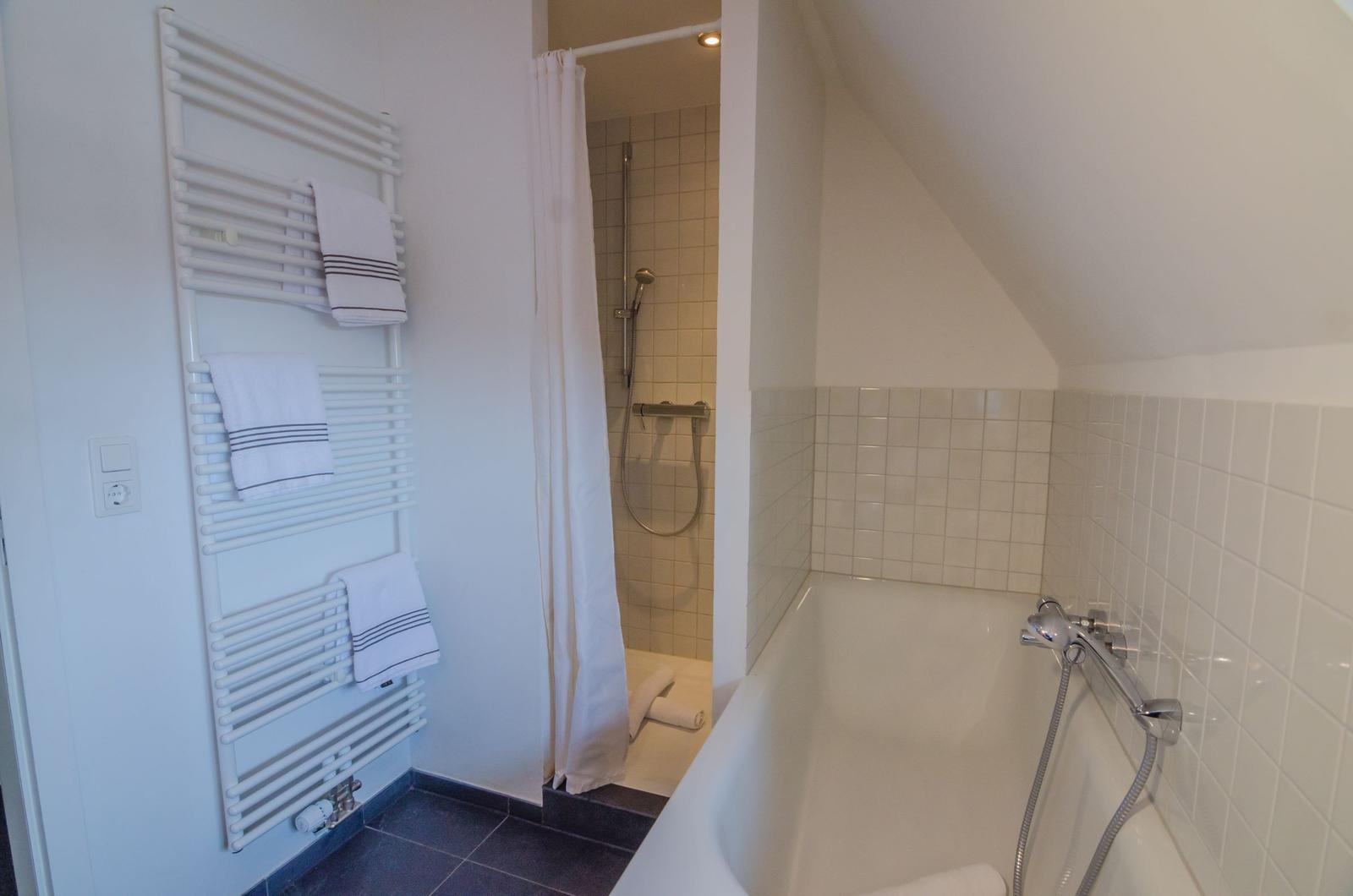 Bathroom with bathtub, shower, and towel warmer with towels.