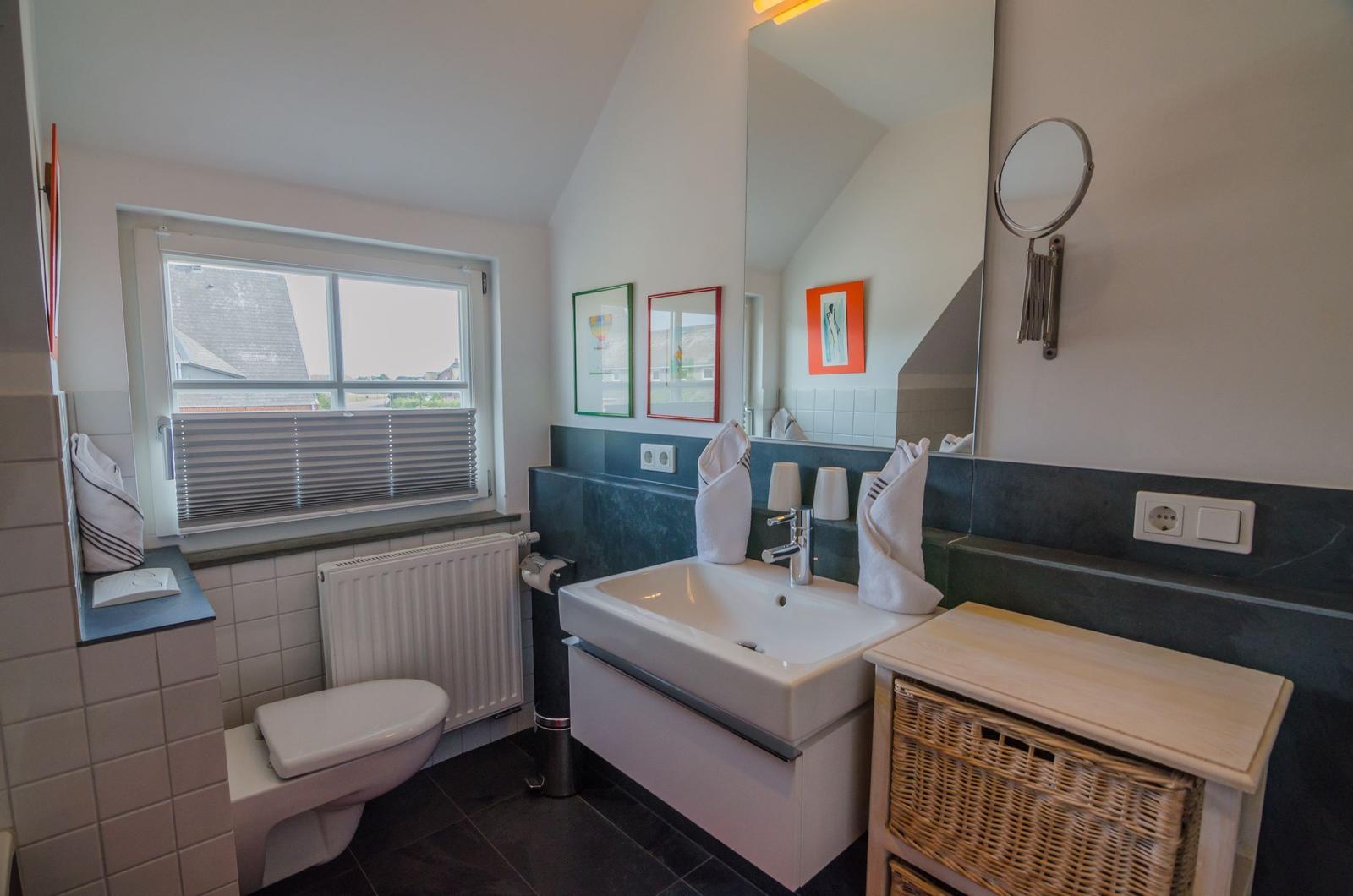 Bathroom with sink, toilet, and window. Wall mirror and basket are present.