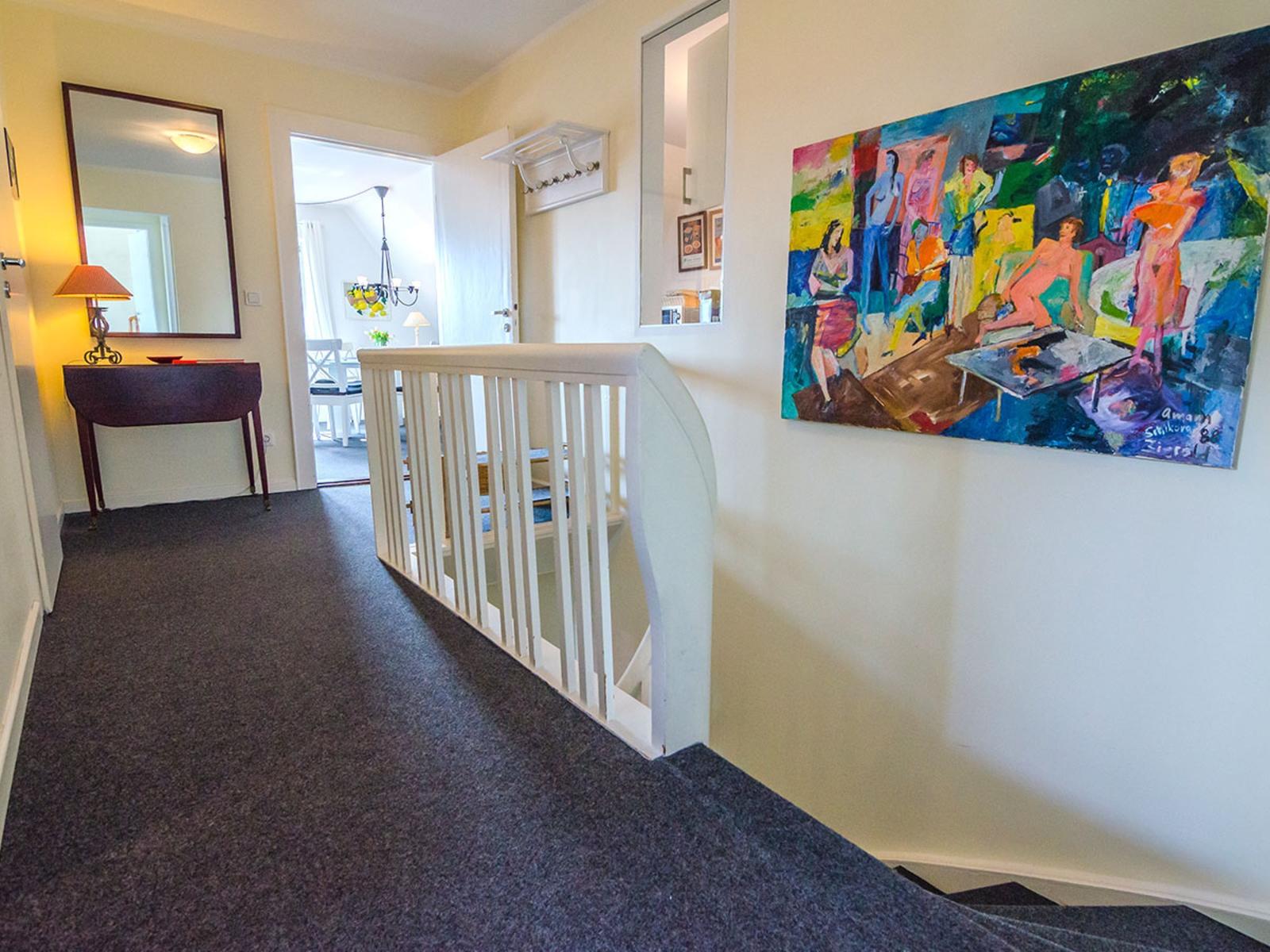 Hallway with wall painting, mirror, and staircase to upper floor.