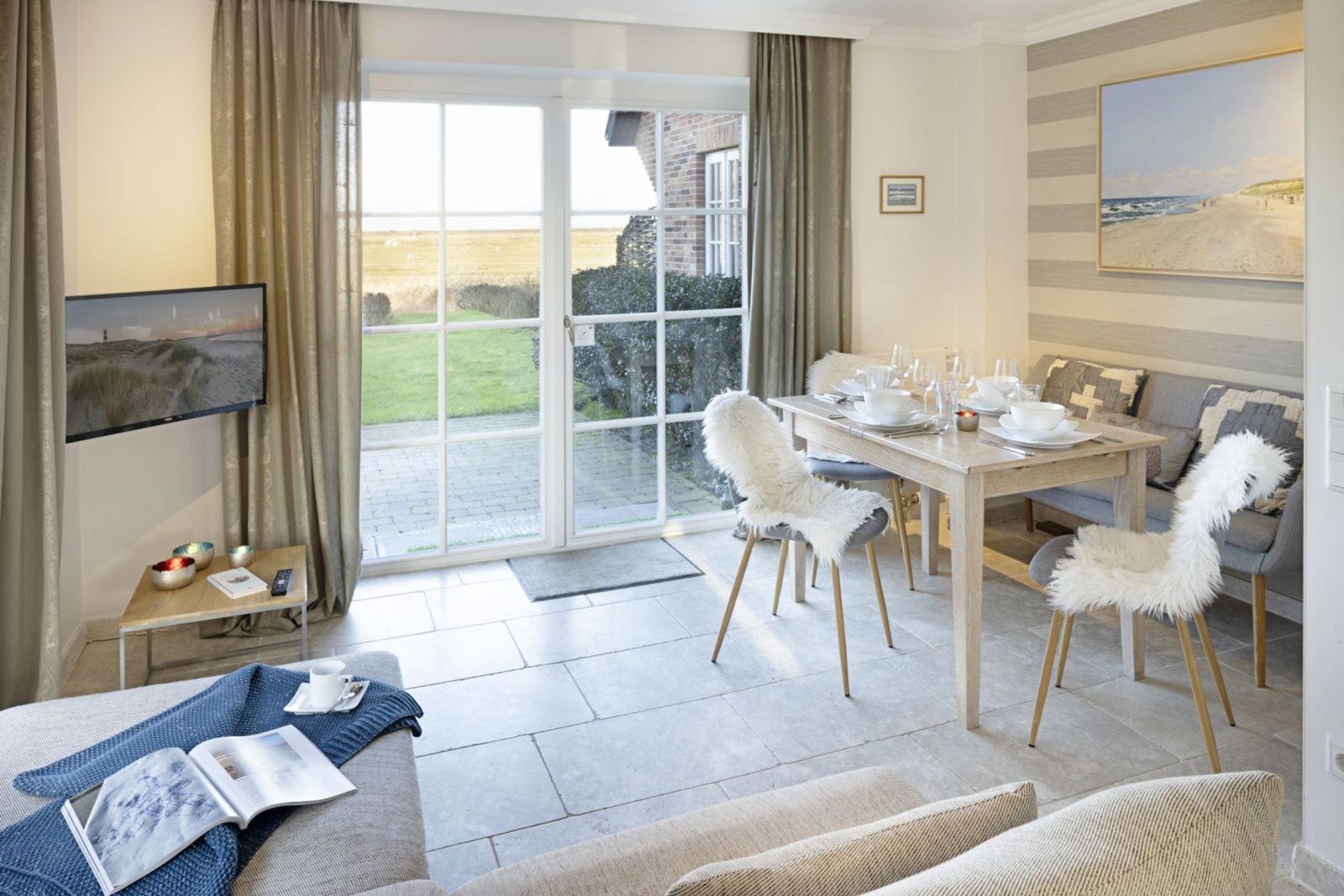 Living and dining area with TV, table, chairs, and view of garden.