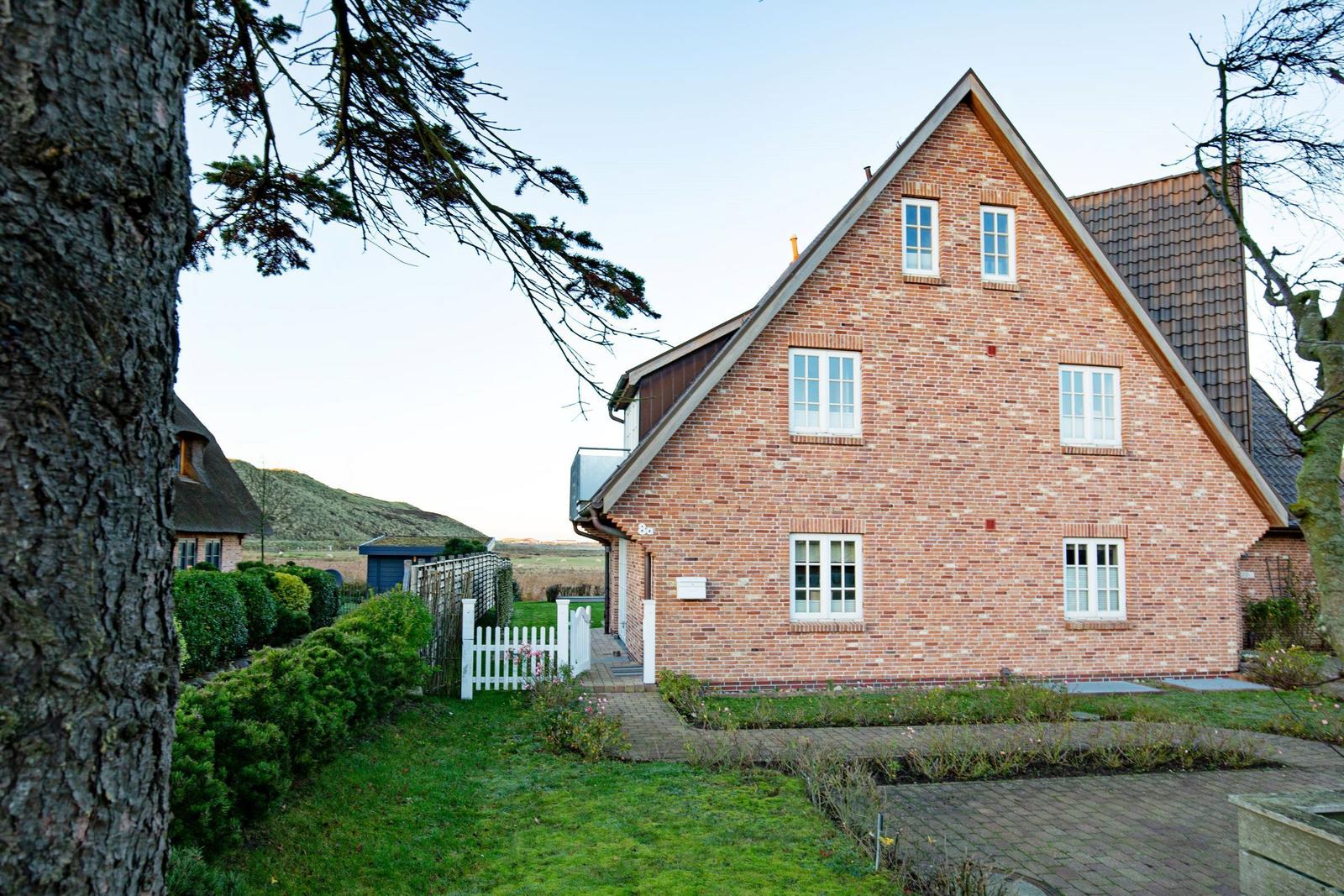 A red brick house with white windows and a paved yard.