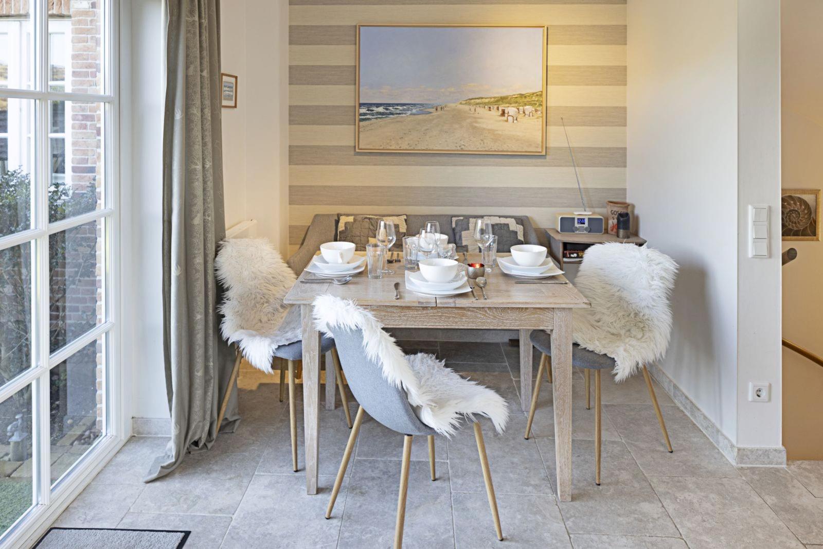 Dining table with four chairs, white fur covers, and beach painting on the wall.