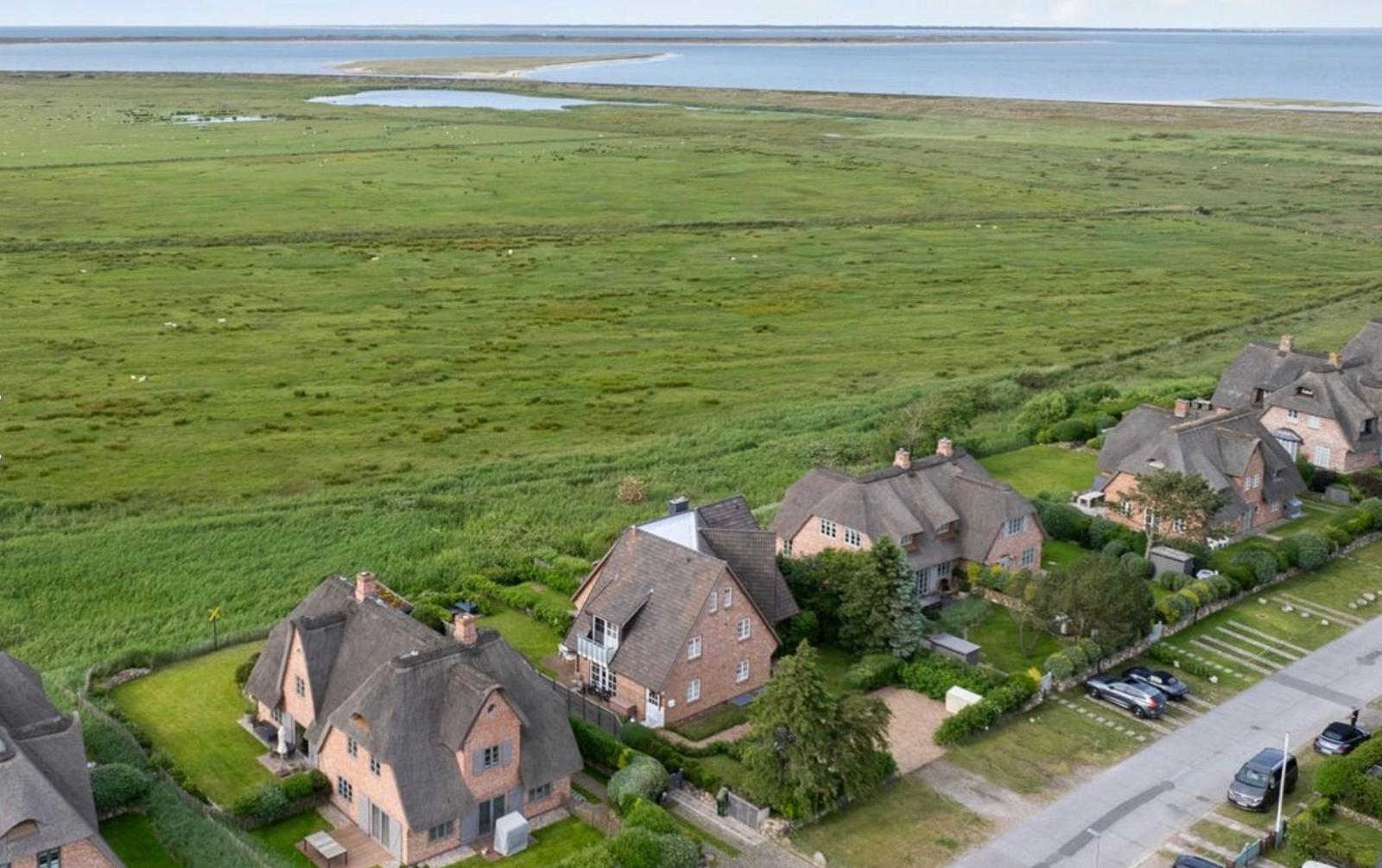Houses with thatched roofs are situated beside a green meadow and directly by the water.