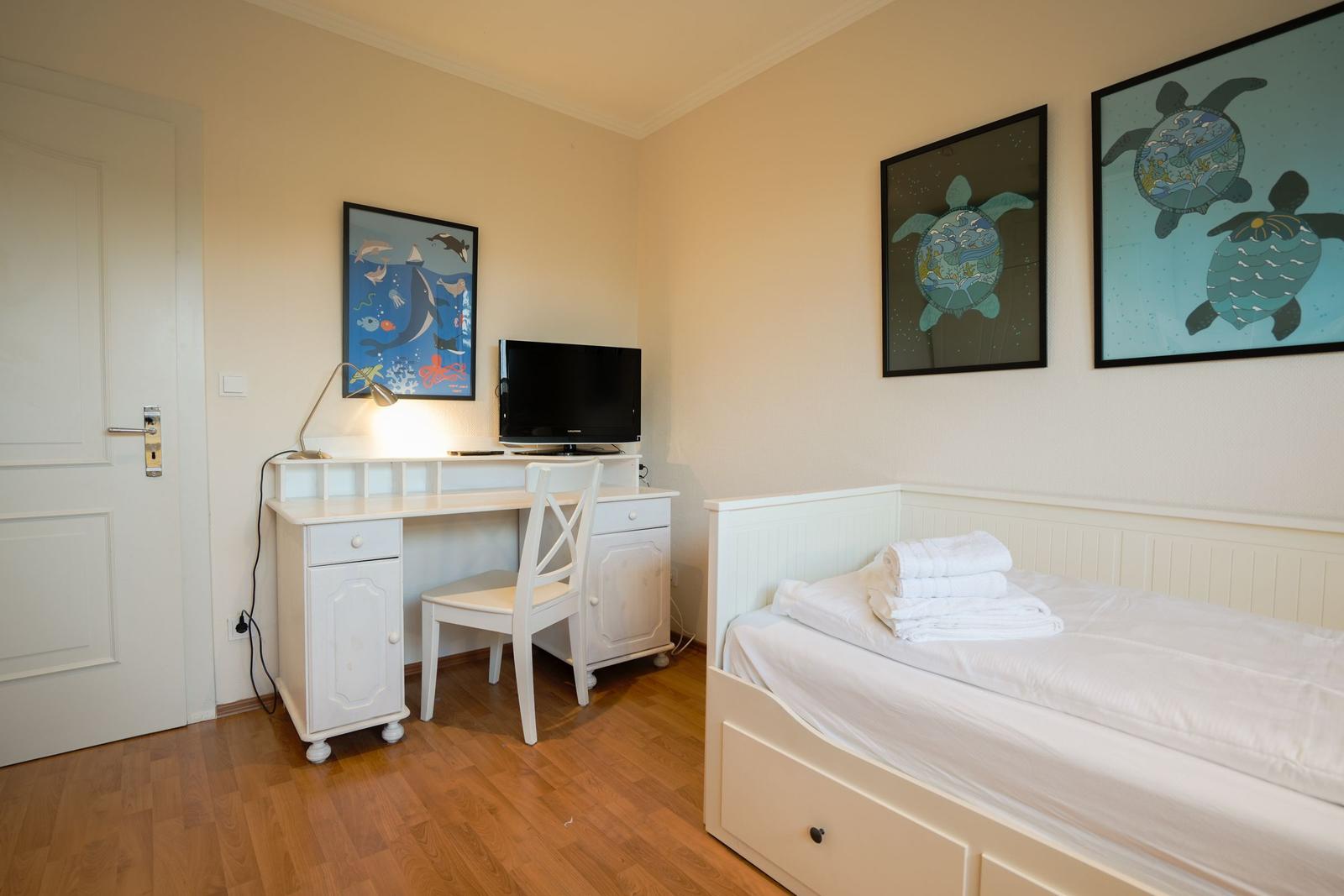 Bedroom with bed, desk, and TV. Wall art features sea animals.