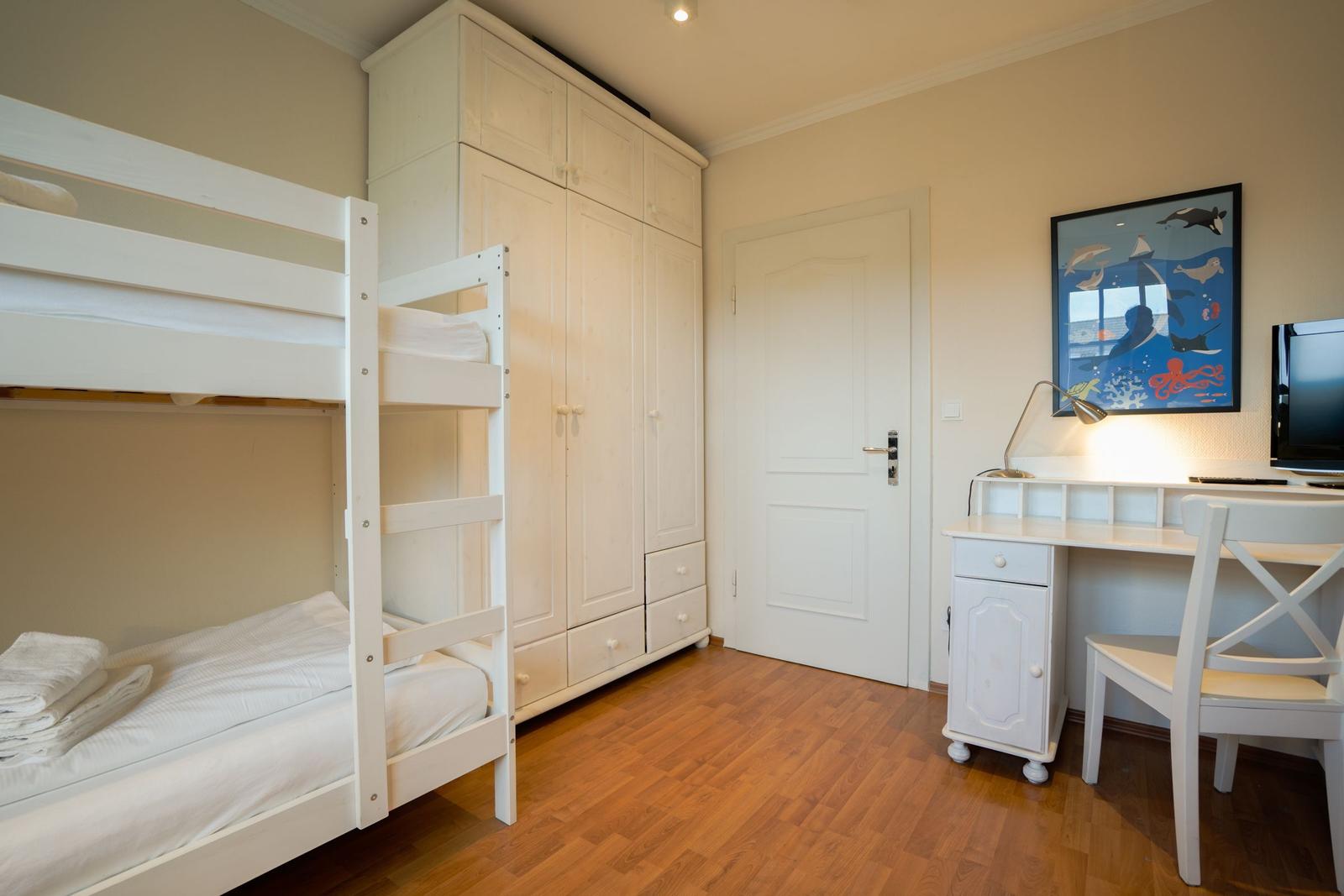 Room with bunk bed, wardrobe, desk, and wall art with sea animals.