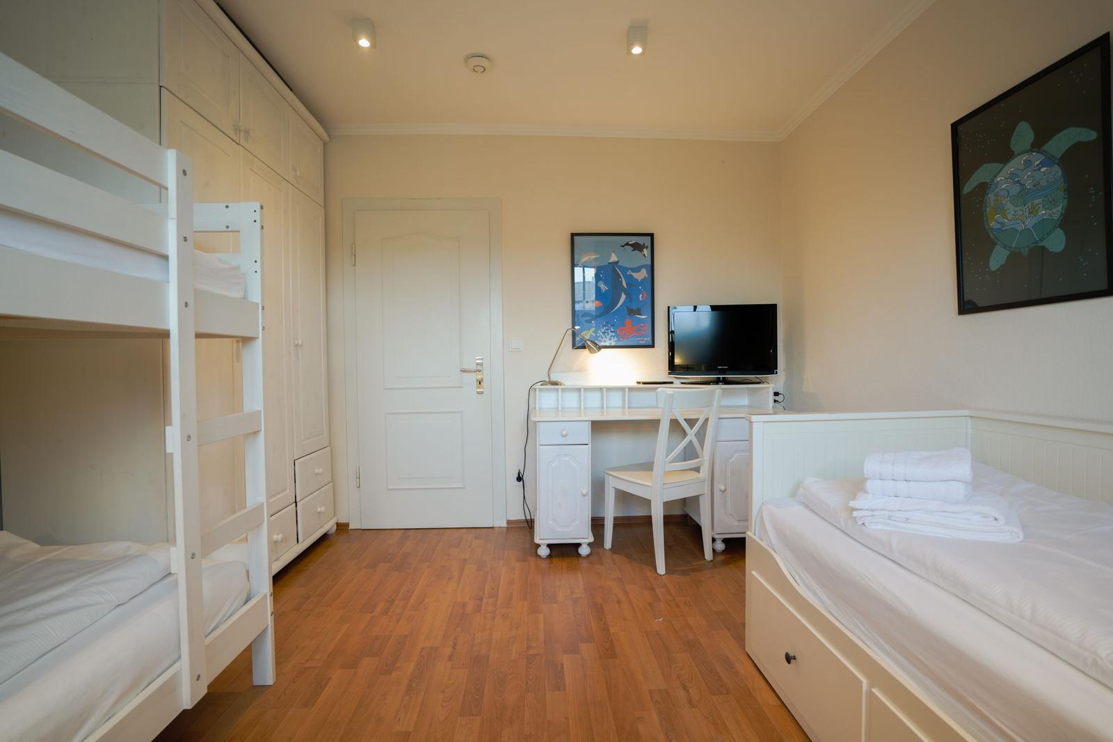 Room with bunk bed, single bed, desk, and TV.