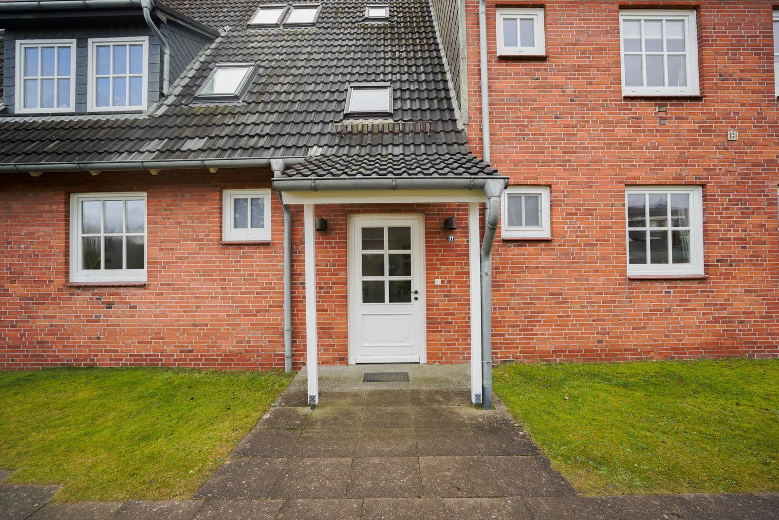 Red brick building with white windows and entrance door. Lawn and stone path in front.