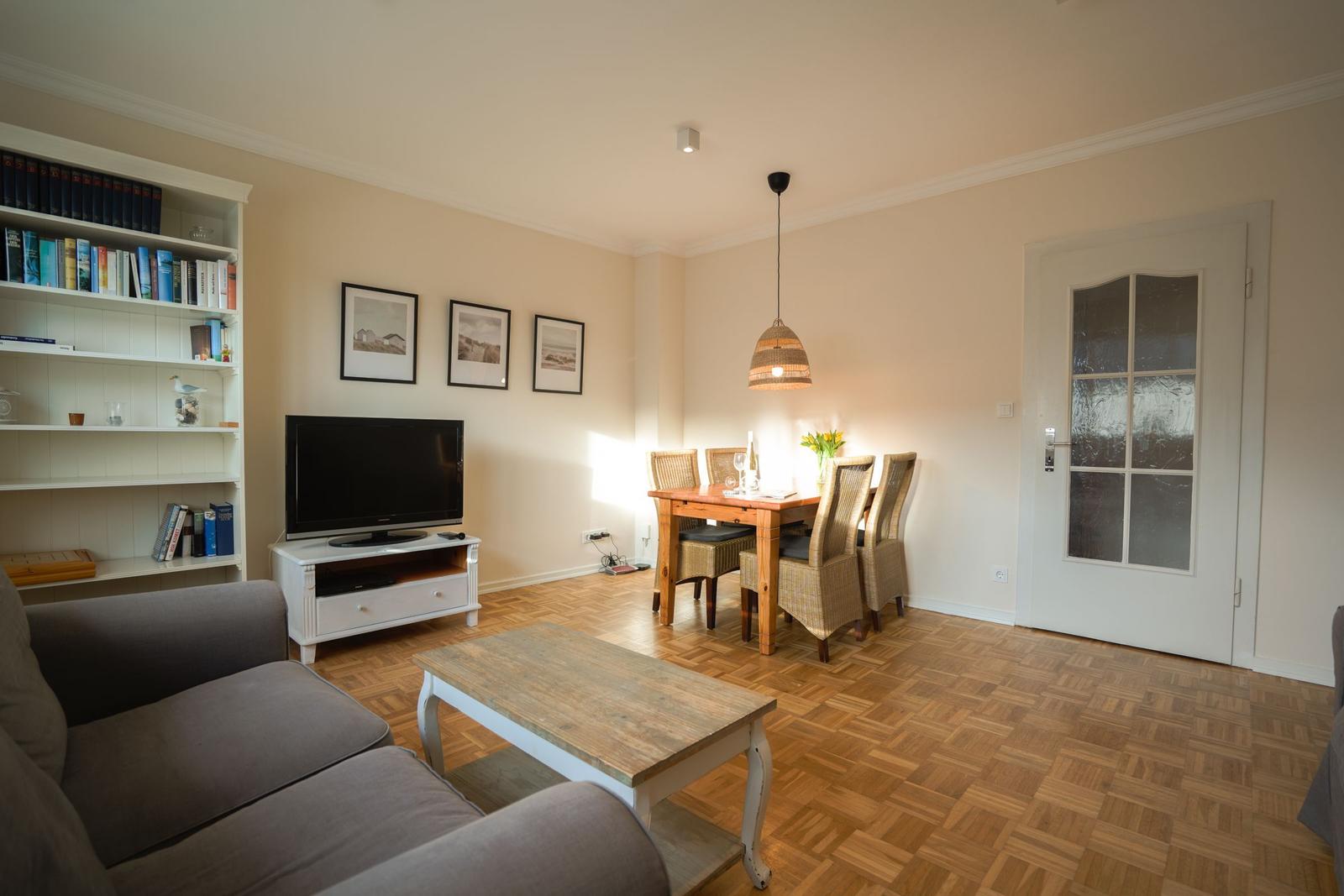 Living and dining area with sofa, TV, table and chairs on parquet floor.