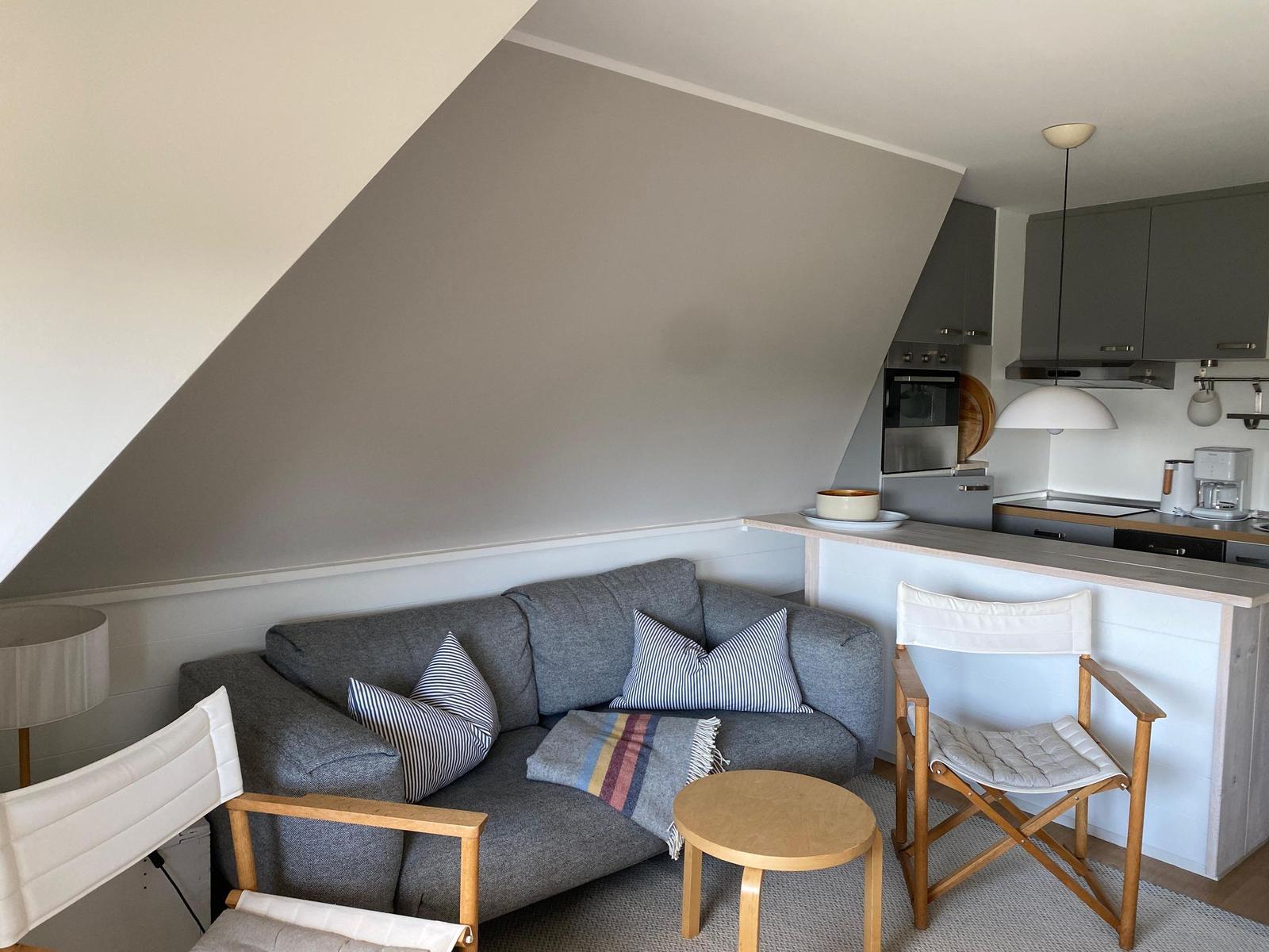 Wohnbereich mit Sofa, Stühlen und Küchenzeile unter Dachschrägen.