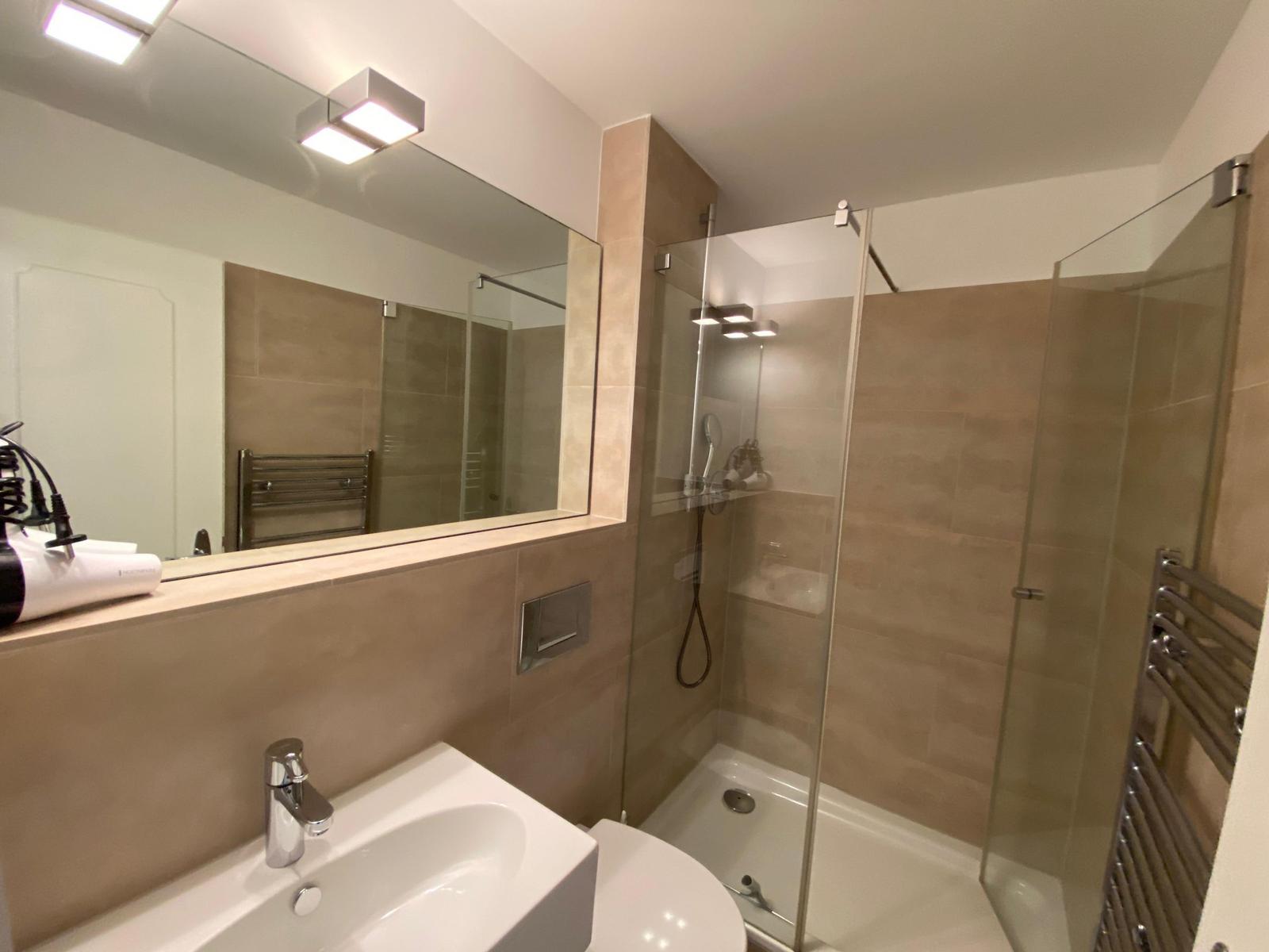 Badezimmer mit Dusche, Waschbecken und Spiegel.