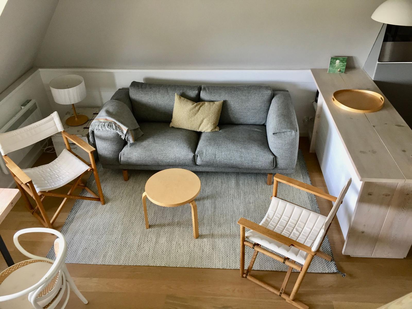 Ein Wohnbereich mit grauem Sofa, zwei Stühlen und einem runden Tisch.