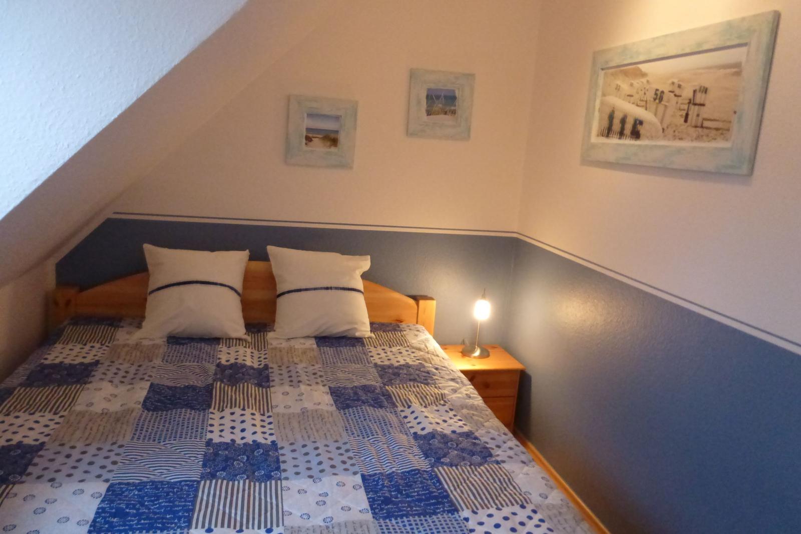 Bedroom with sloped ceiling, bed with pillows, and nightstand with lamp.