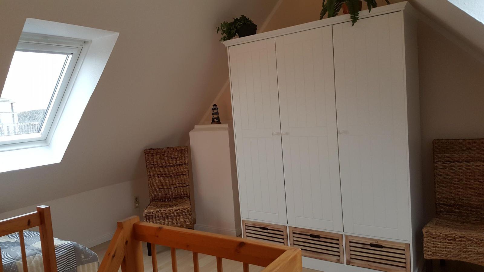 Bedroom with sloped ceiling, window, wardrobe, and chair.