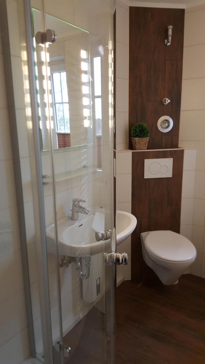 Bathroom with shower, sink, and toilet. Wooden wall and mirror with lighting.