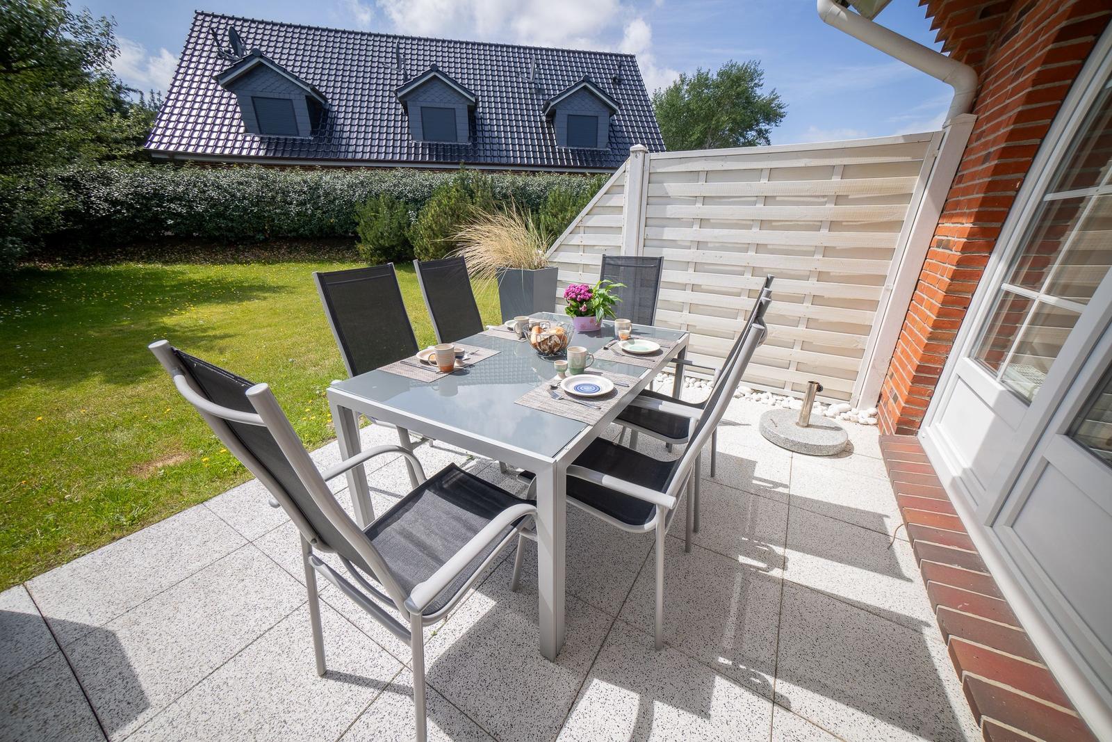 Terrasse mit Tisch und Stühlen, Garten und Haus im Hintergrund.