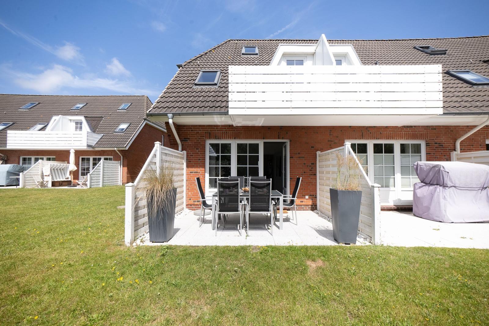 Terrasse mit Tisch und Stühlen vor einem Haus mit Garten.
