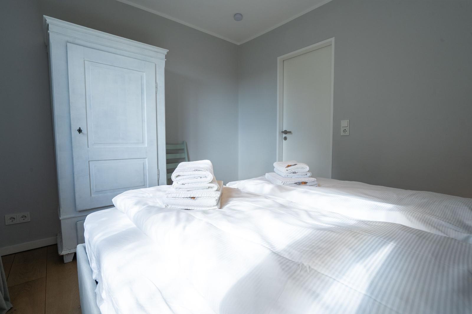Bedroom with bed, white wardrobe, and folded towels.