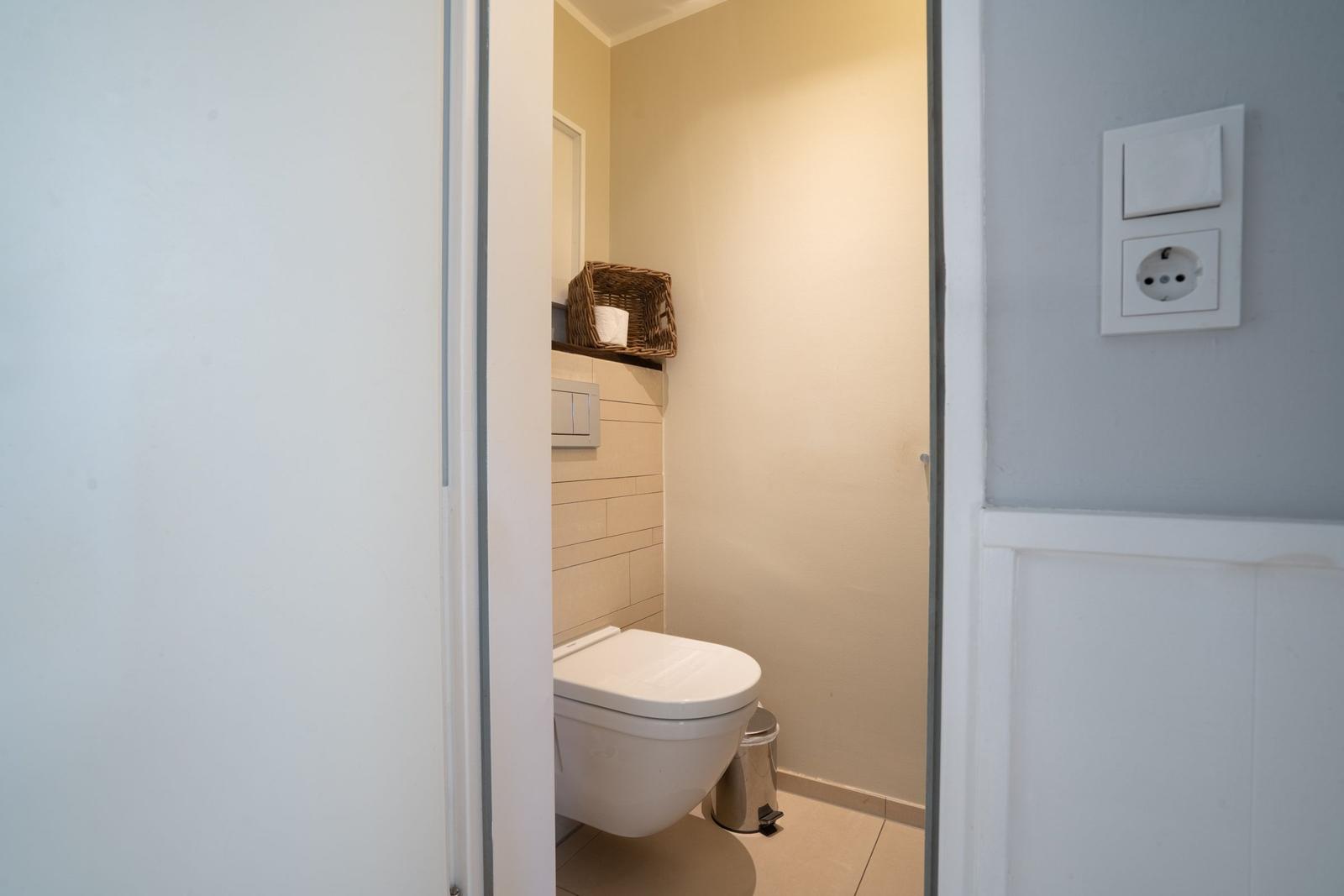 Behind the door, a toilet with a basket and trash can is visible.