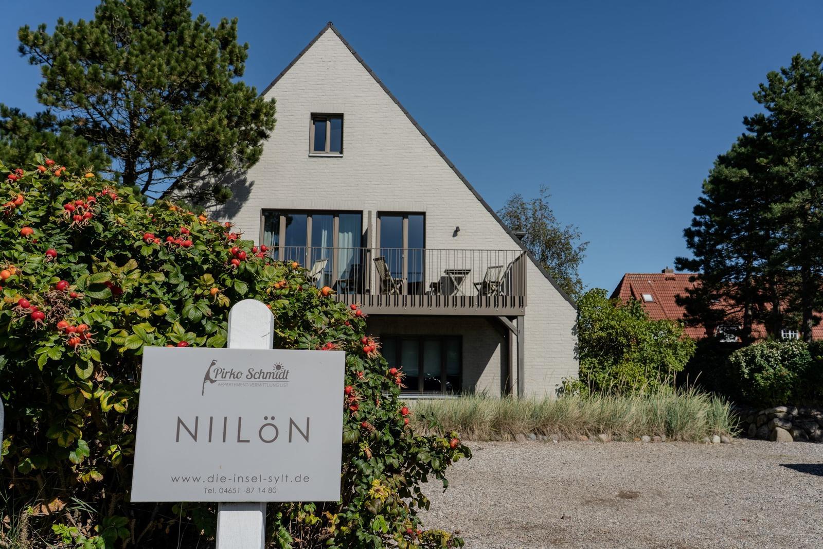 Modern villa with balcony and sign NIILÖN. Surrounded by trees and shrubs.