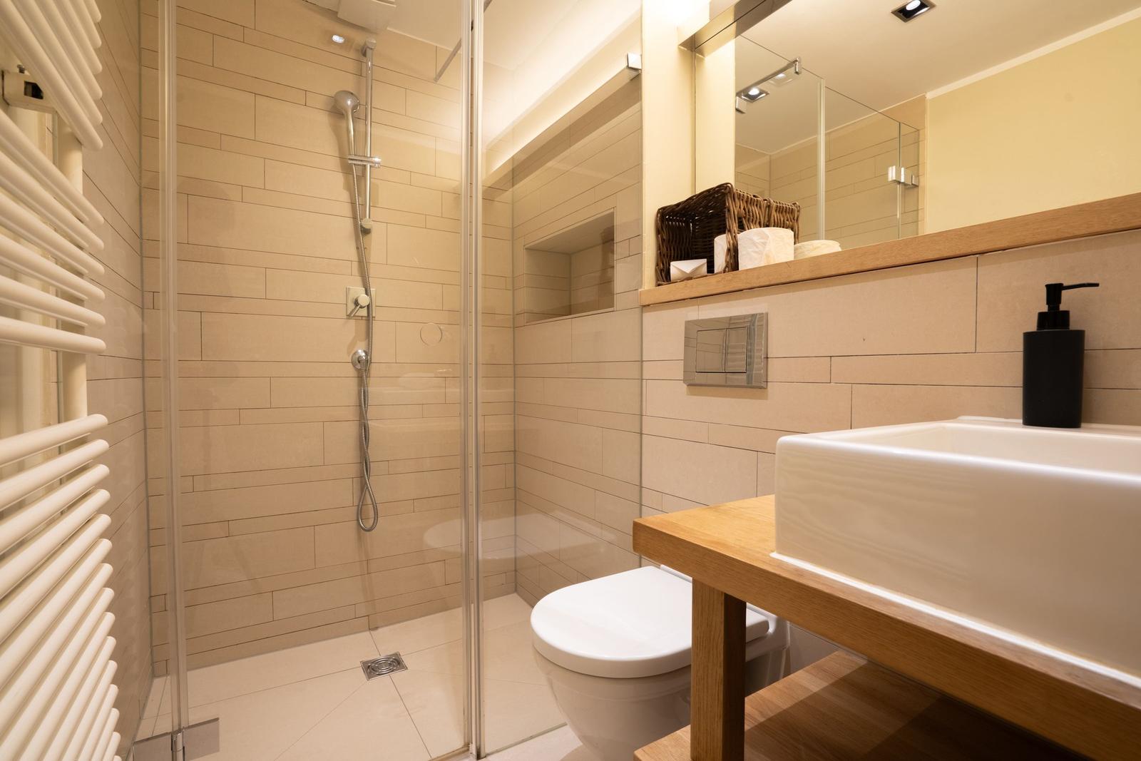 Shower with glass enclosure, sink with wooden vanity, and toilet.