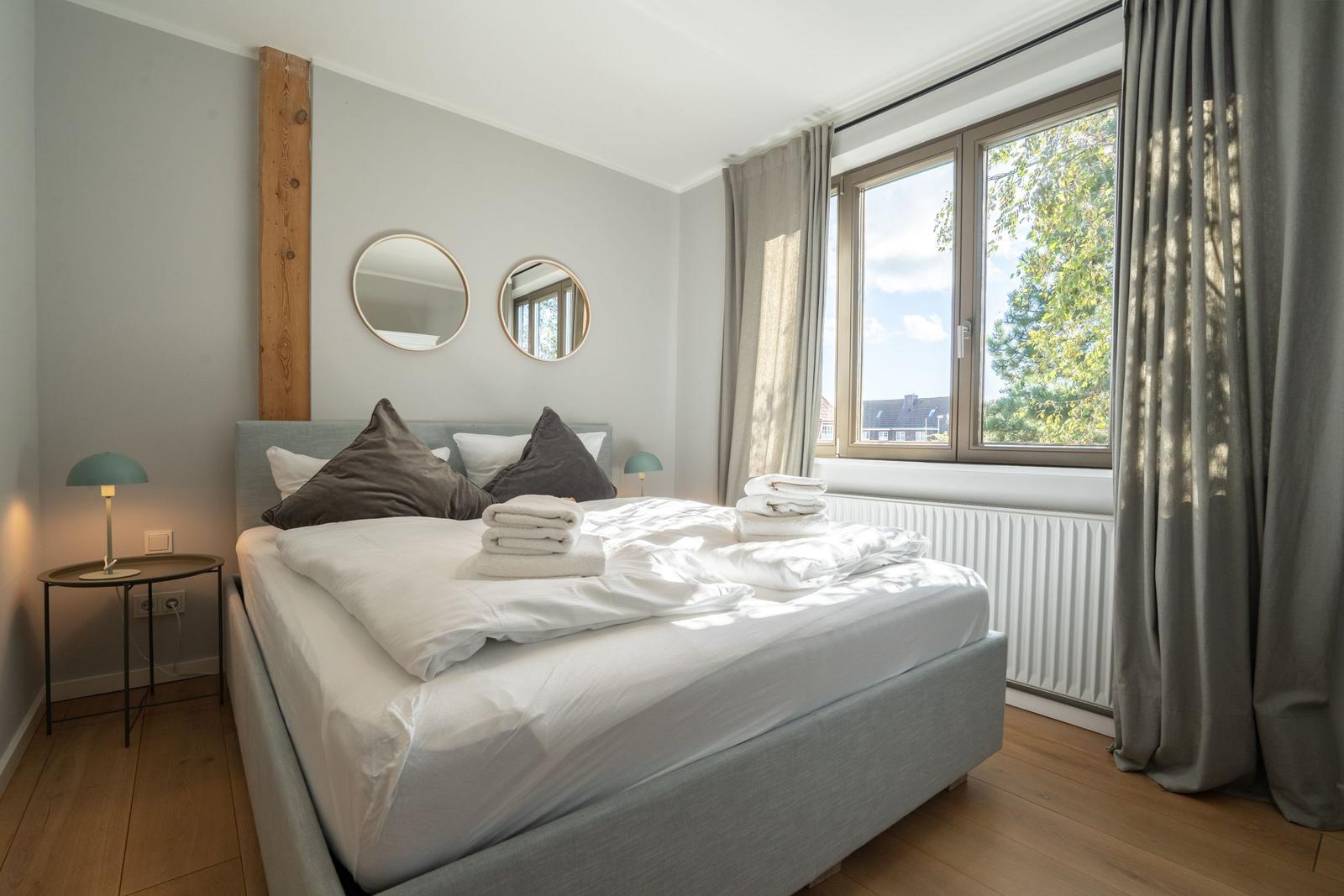 Bedroom with bed, two round mirrors, and window with view of trees.