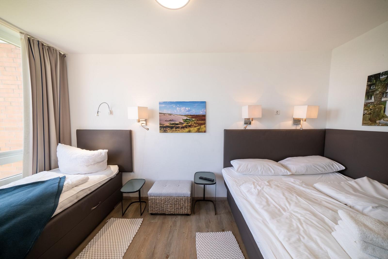 Room with two beds, wall lamps, and pictures on the walls.