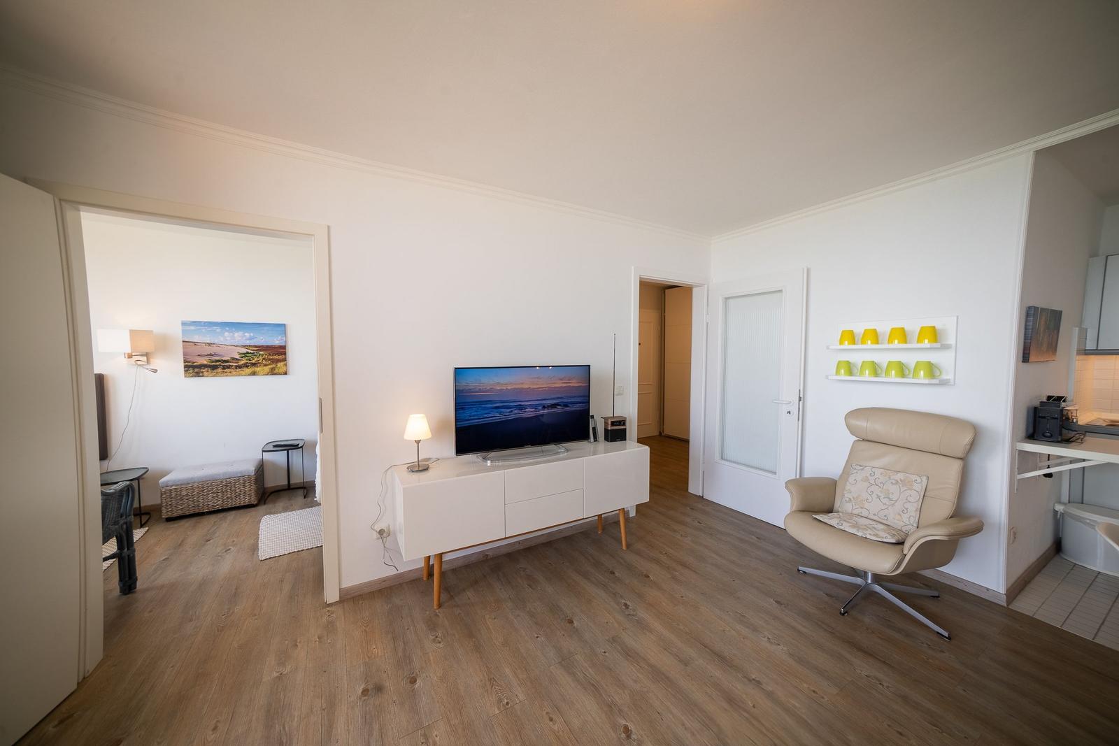 Living room with TV, armchair, and kitchen area.