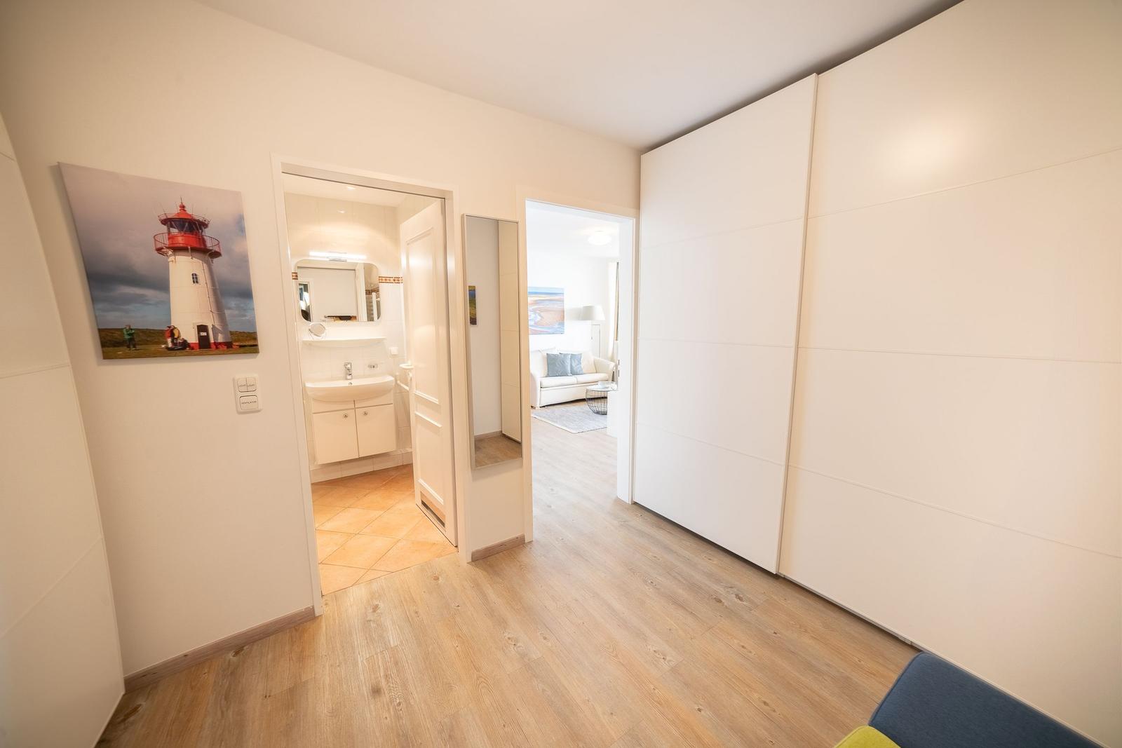 Hallway with bedroom, bathroom, and living room. Wall picture shows a lighthouse.