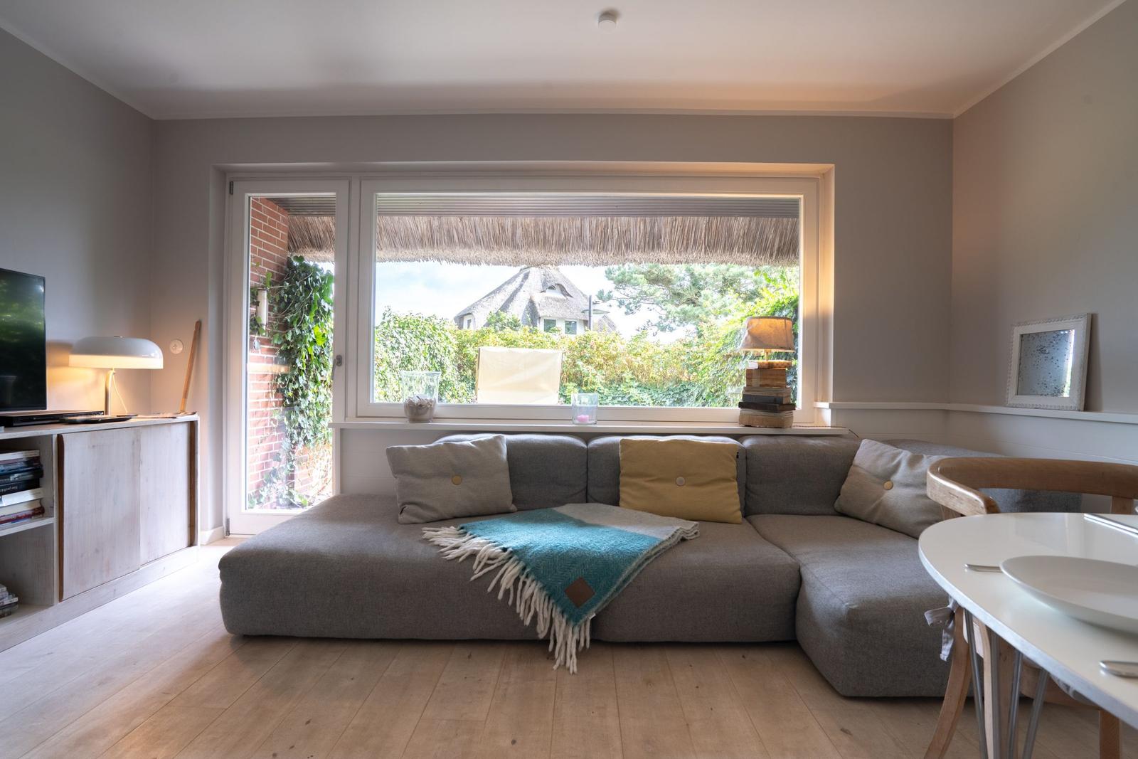Wohnzimmer mit Sofa, Fenster und Blick auf grüne Umgebung.