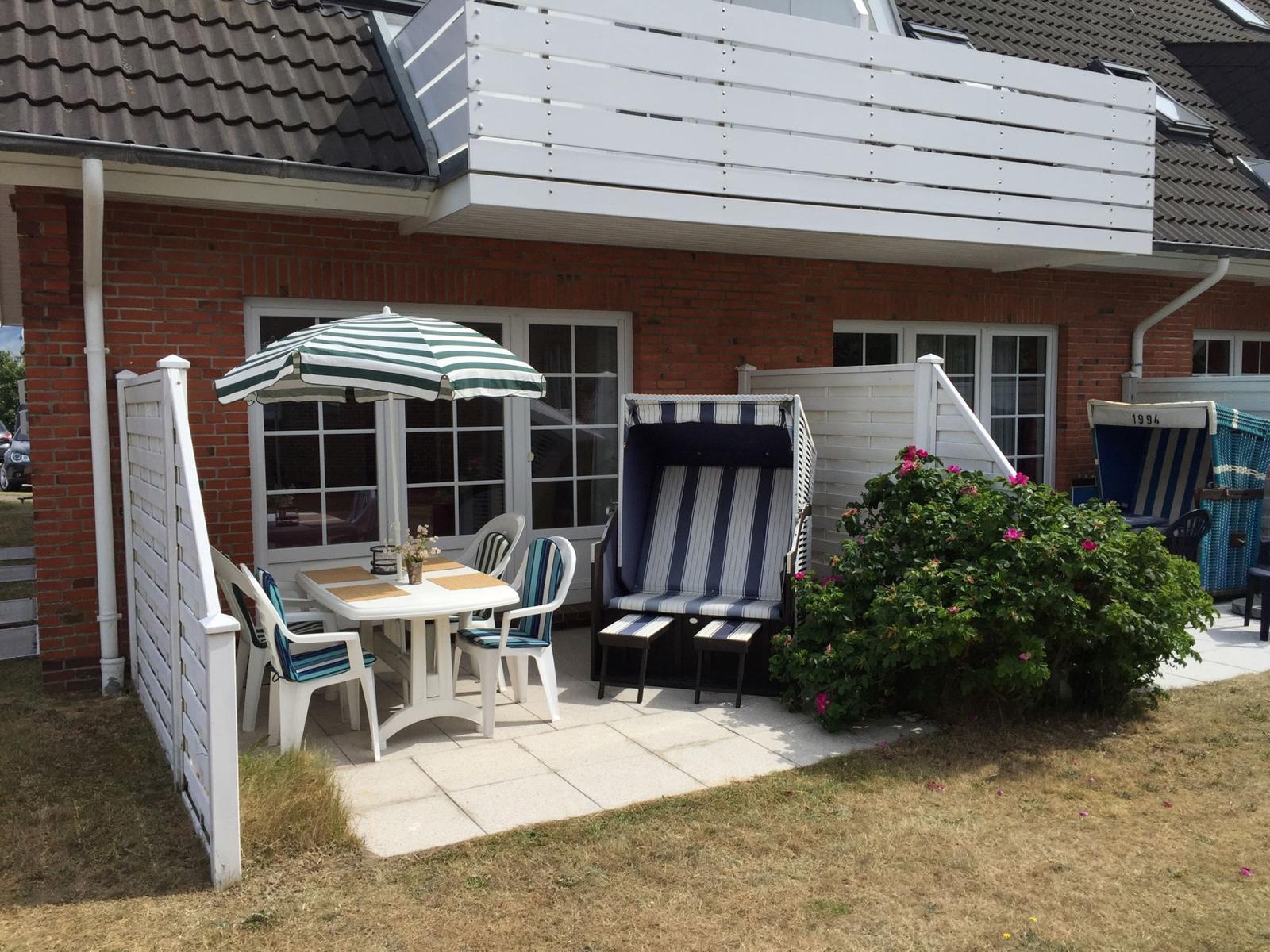 Terrasse mit Tisch, Stühlen und Sonnenschirm neben Strandkörben.