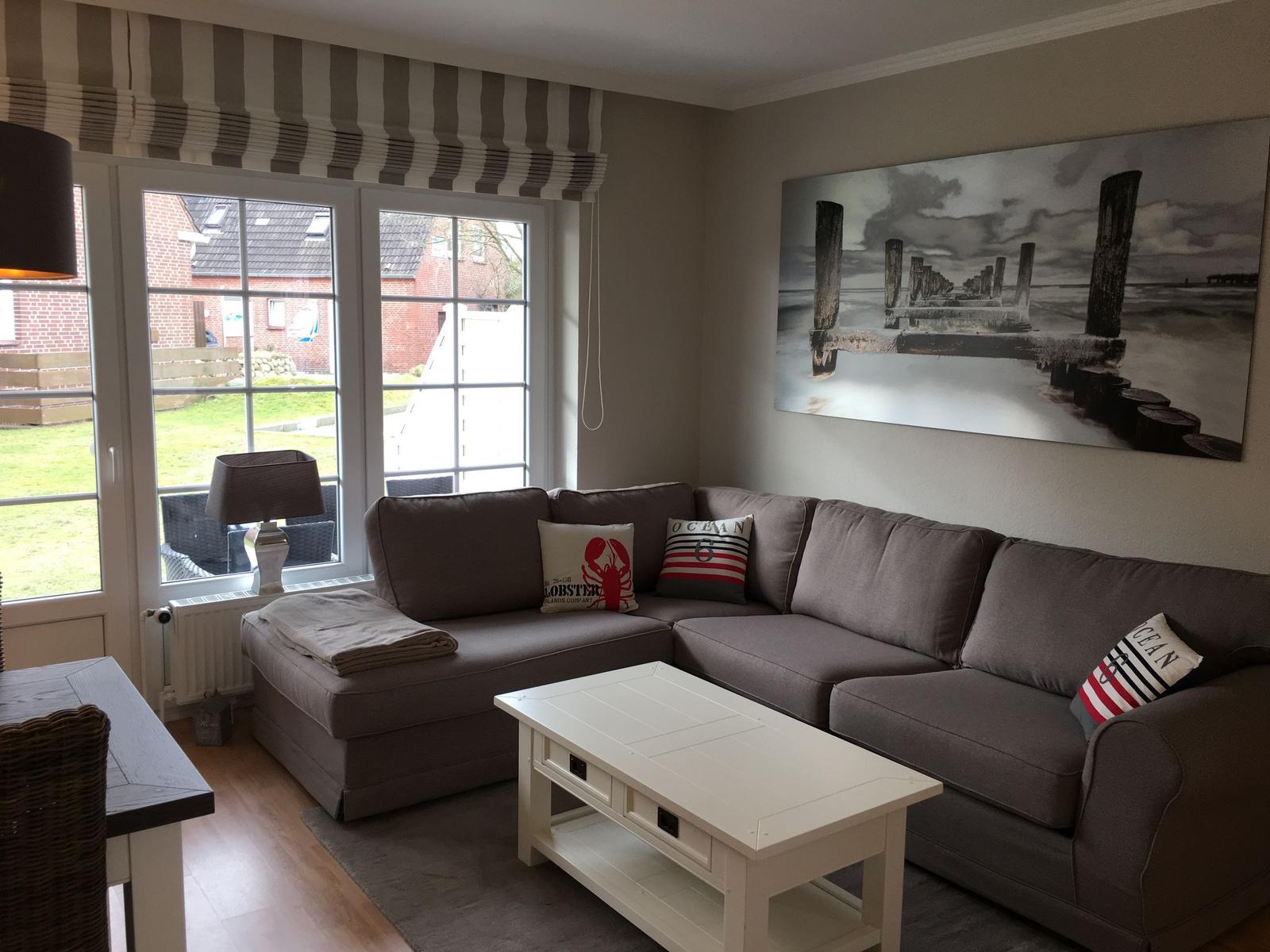 Ein Wohnzimmer mit grauem Sofa, weißem Tisch und Fenster zur Außenseite.