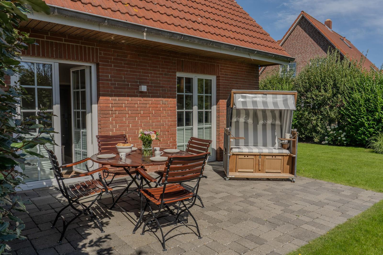 Terrasse mit Tisch, Stühlen und Strandkorb. Hinterhof mit Rasen und Ziersträuchern.